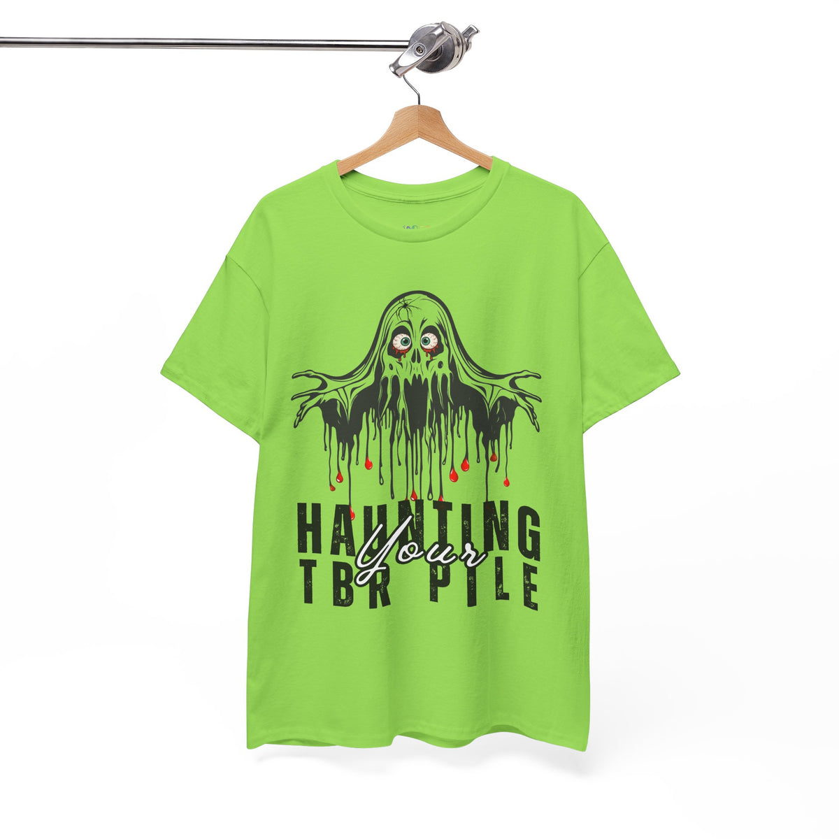 A bright lime green short-sleeve t-shirt hanging on a wooden hanger from a metal rail. The shirt features a black dripping slime monster graphic with red eyes and the text 'HAUNTING YOUR TBR PILE' in black and white.