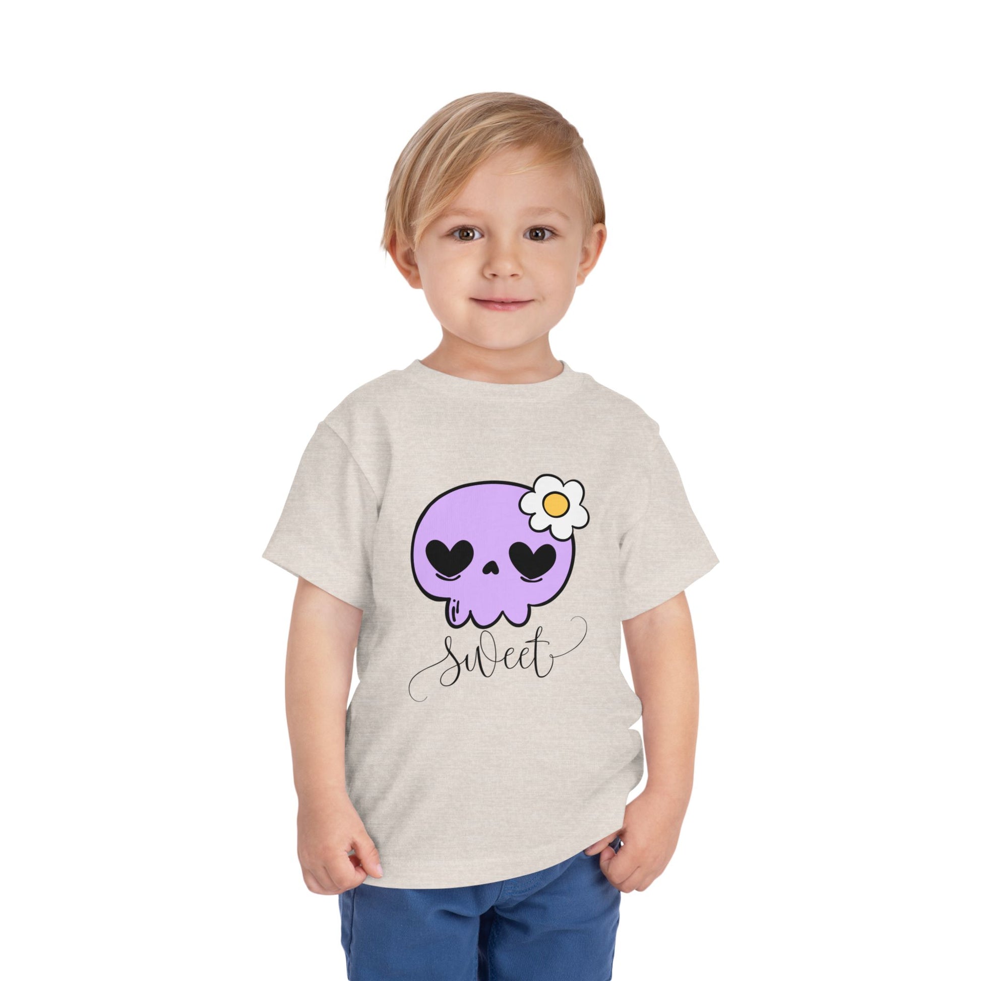 Child wearing a tan toddler t-shirt with a purple skull design and the word 'sweet' 