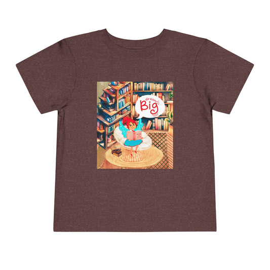 Maroon t-shirt with a colorful library graphic of a fairy reading a book and thought bubble text 'Dream Big'