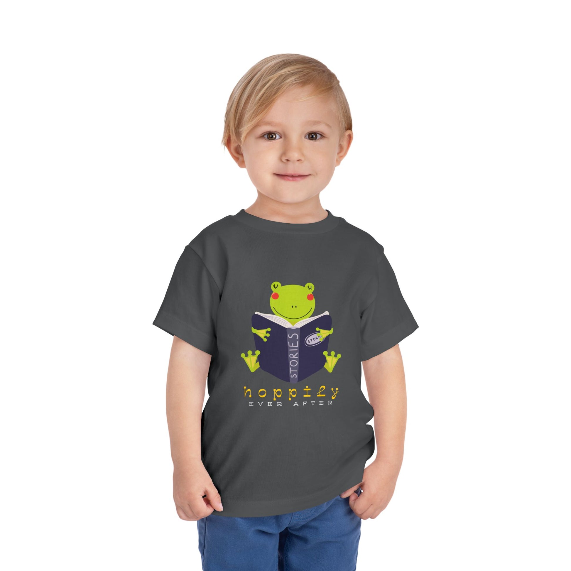 Child wearing a gray toddler t-shirt with a frog reading a book graphic and text 'Hoppily Ever After'
