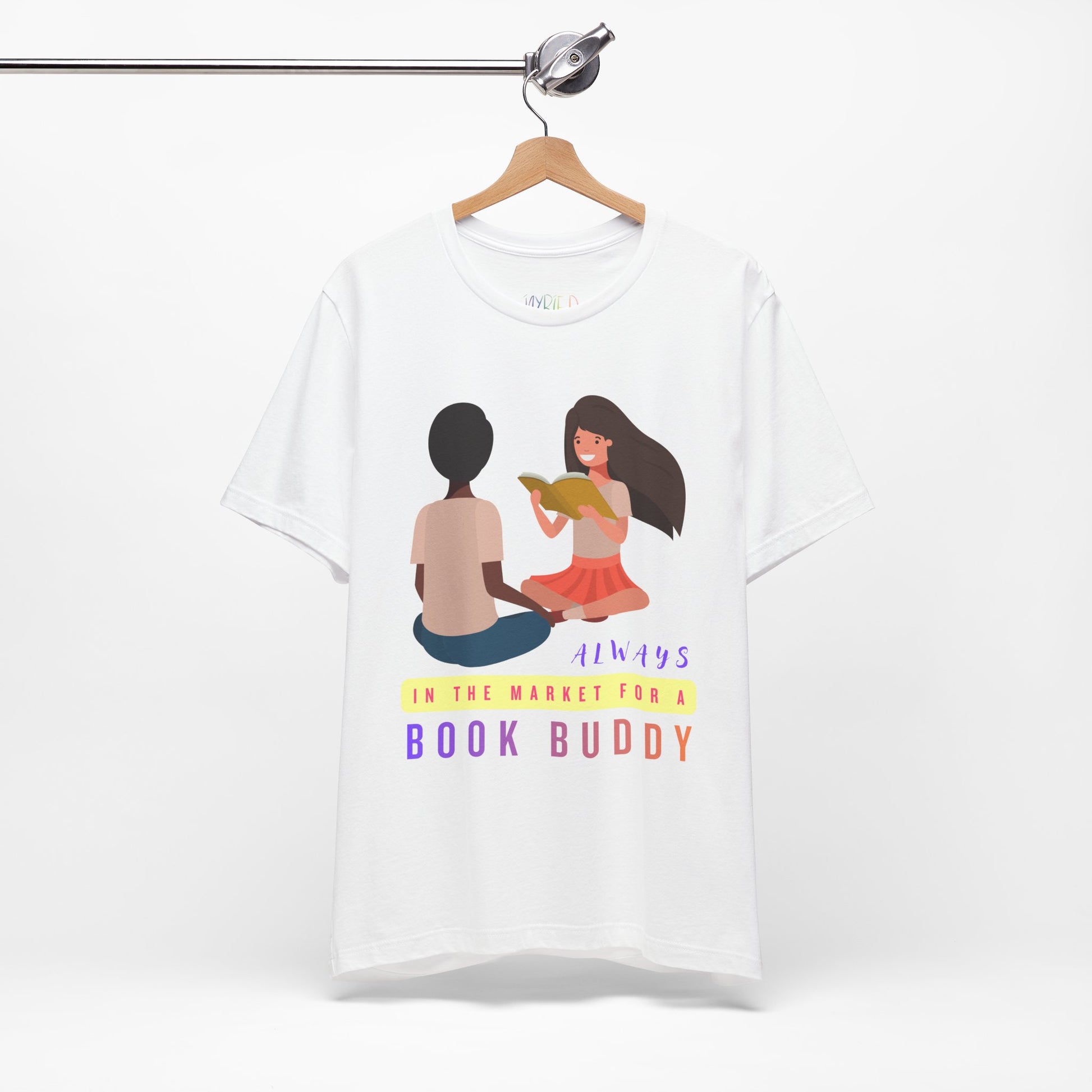White t-shirt with graphic of two people reading together and text 'Always in the market for a book buddy' 