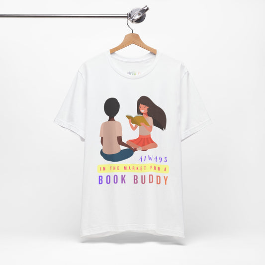White t-shirt with graphic of two people reading together and text 'Always in the market for a book buddy' 