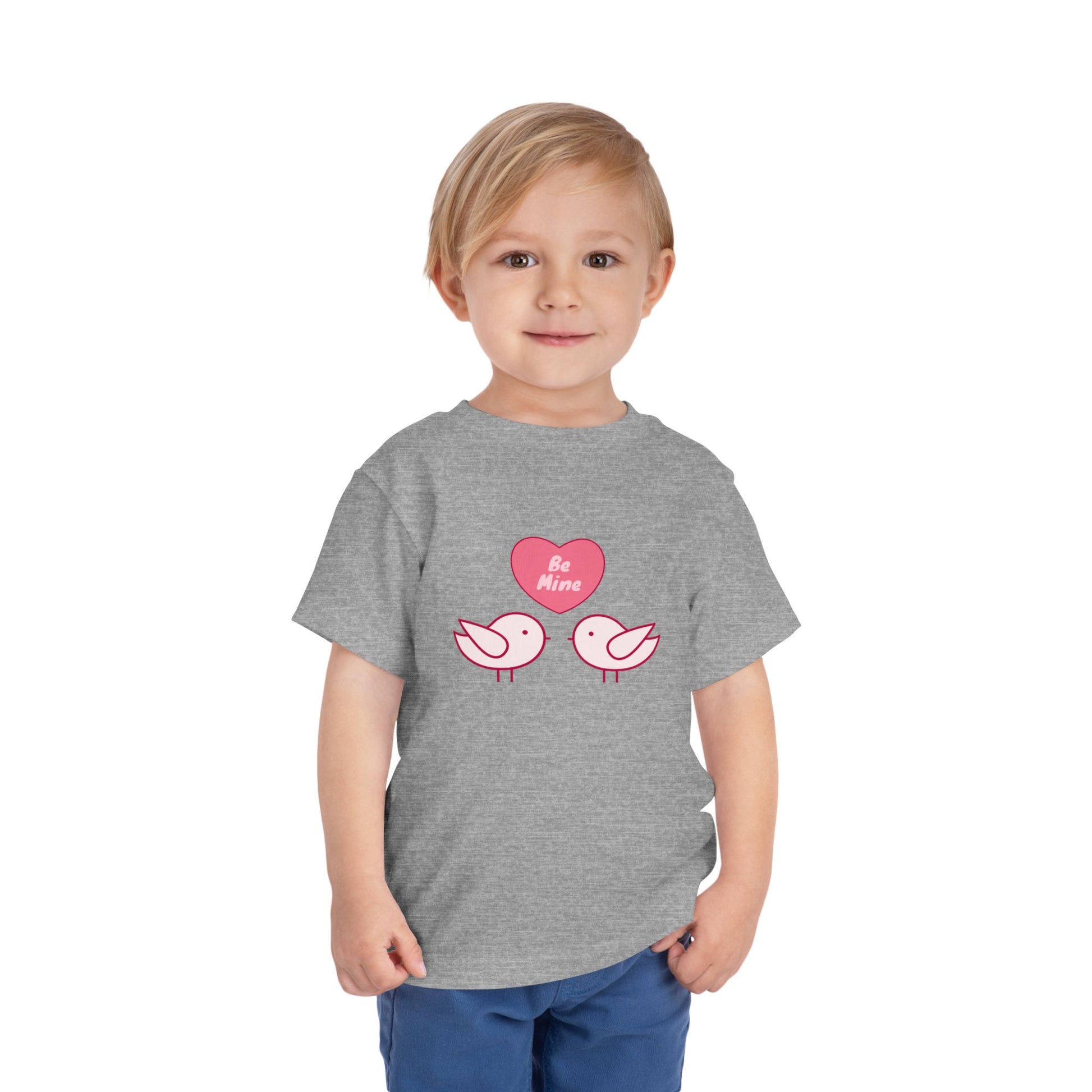 Child wearing a gray toddler t-shirt with pink heart, two pink birds and 'Be Mine' text 