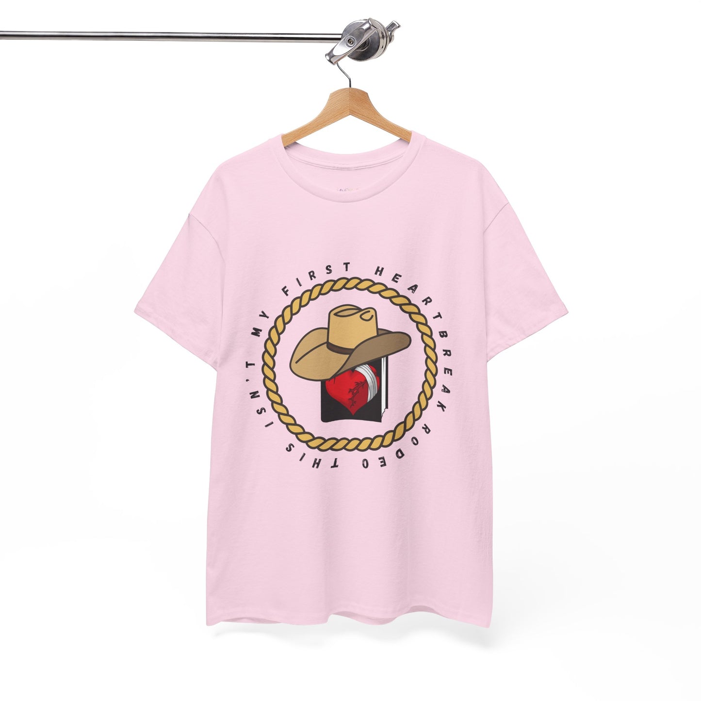Pinkt-shirt with a cowboy hat atop a book with a broken heart, circled by a rope and text 'This Isn't My First Heartbreak Rodeo'
