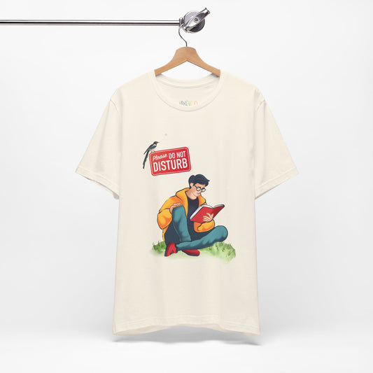 Beige t-shirt with a graphic of a person sitting in the grass reading a book, and a bird perched atop a 'Do Not Disturb' sign