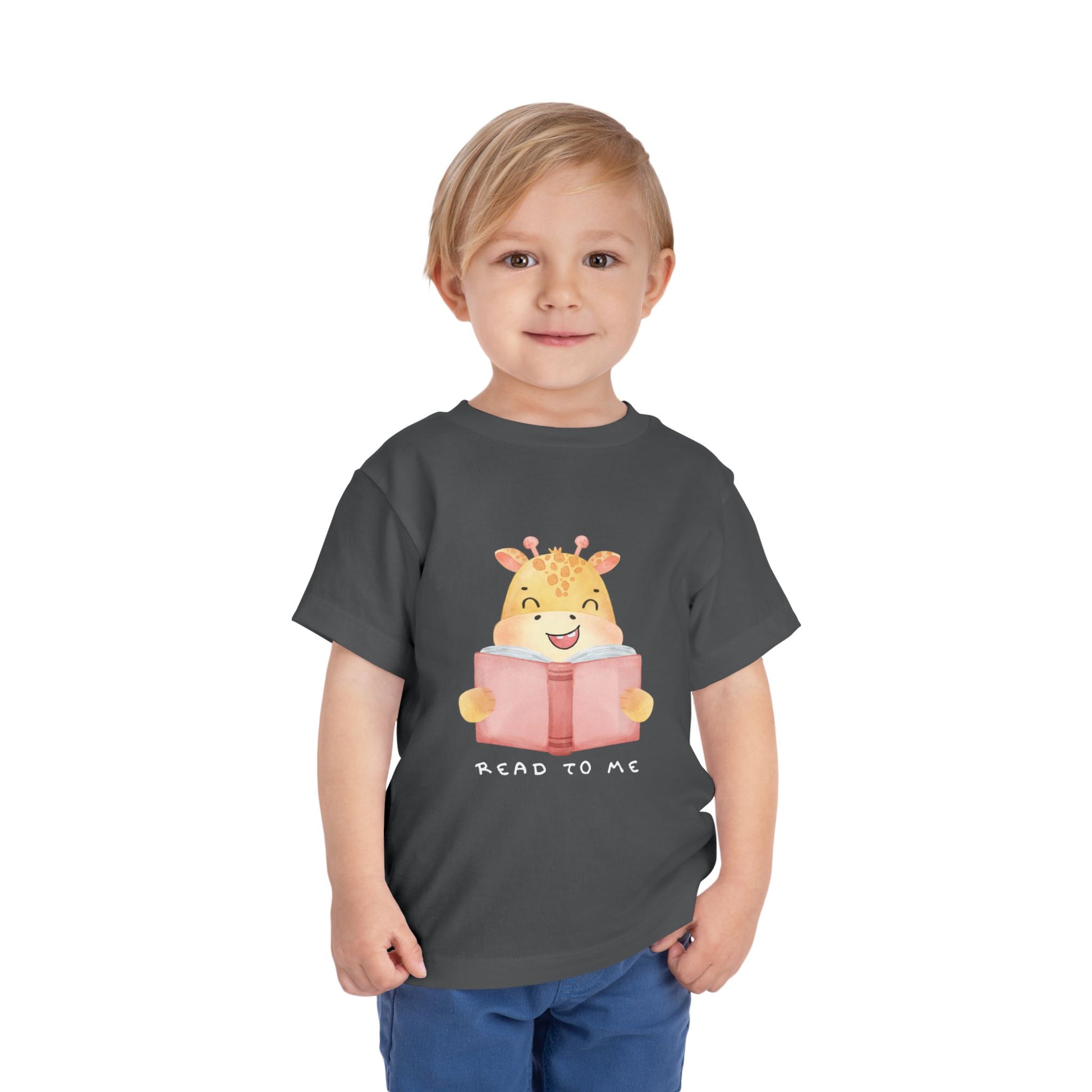Child wearing a gray toddler t-shirt with a giraffe reading a book graphic and 'Read to Me' text 