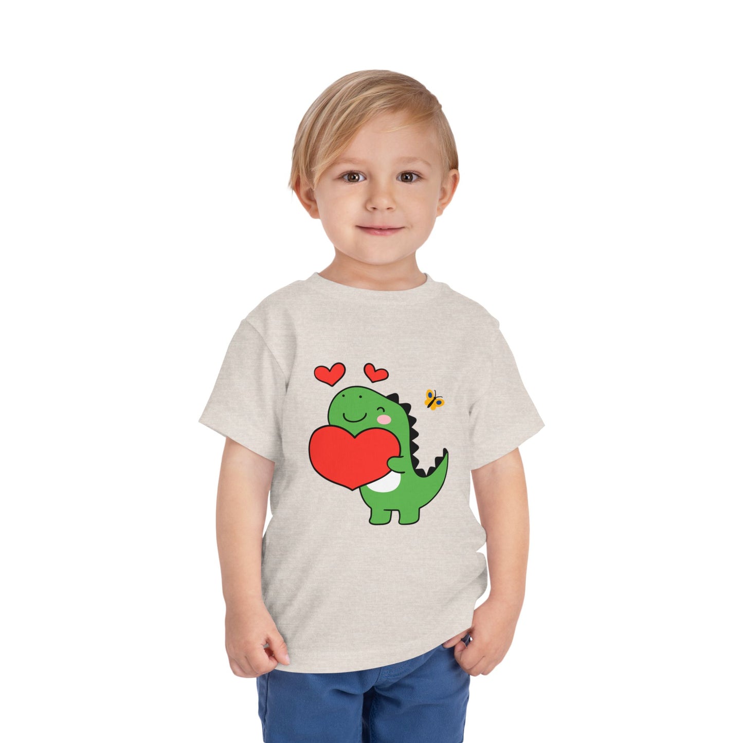 Child wearing a beige toddler t-shirt with a cartoon dinosaur hugging a red heart