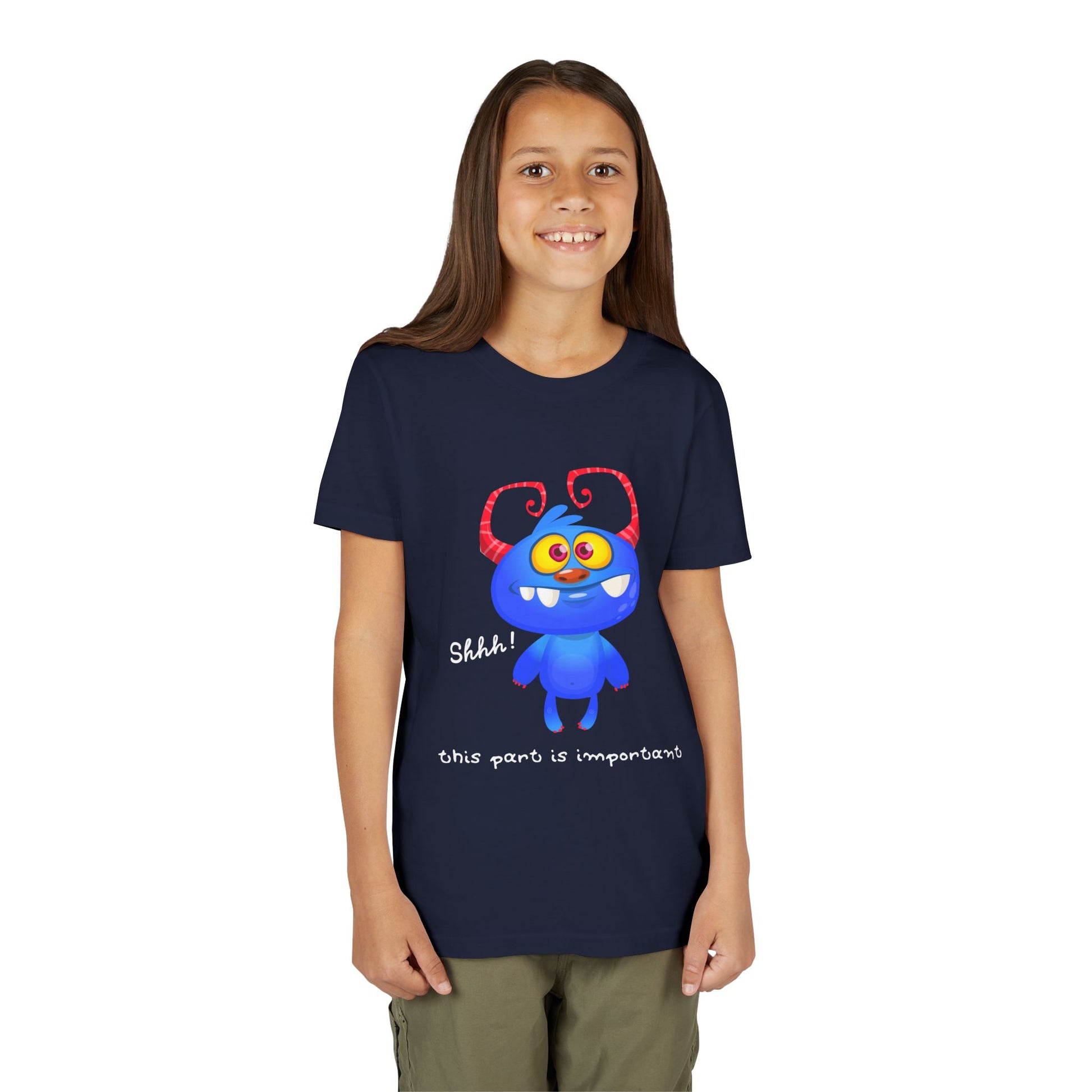 Girl wearing a navy blue t-shirt with a wide-eyed, gap toothed, blue cartoon monster and text 'Shhh! This part is important.'