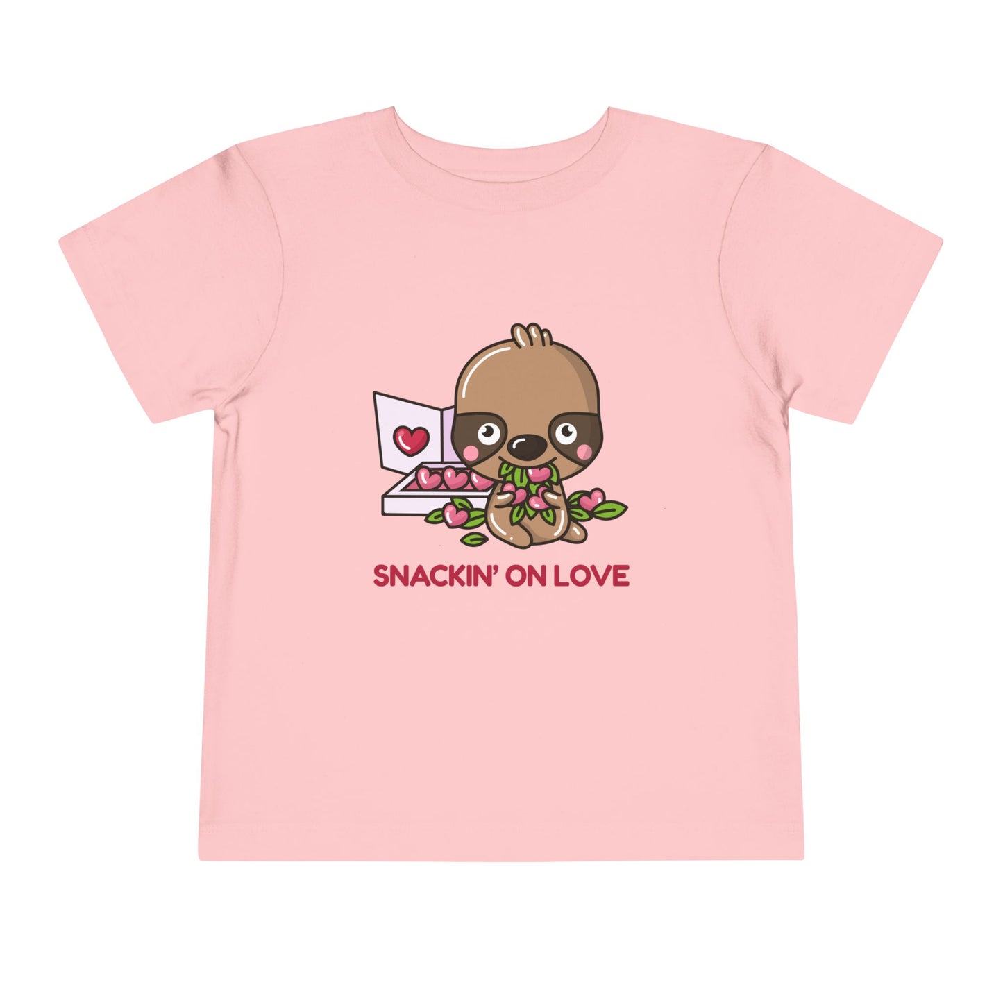 Pink toddler t-shirt with a cartoon eating a box of heart shaped candies, text 'SNACKIN' ON LOVE'