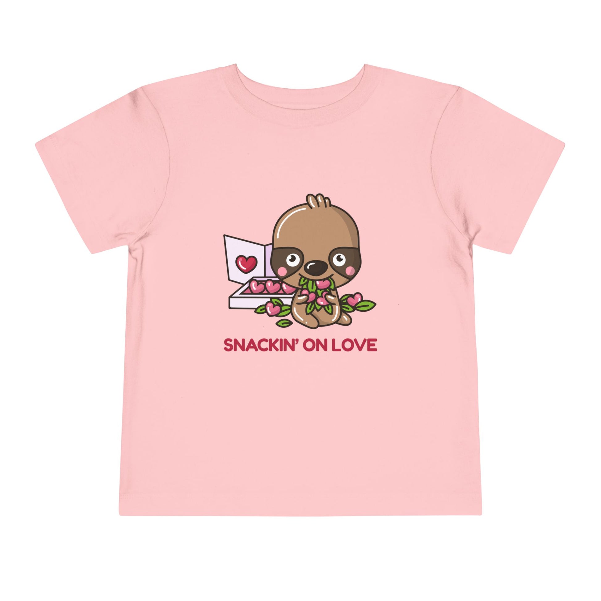 Pink toddler t-shirt with a cartoon eating a box of heart shaped candies, text 'SNACKIN' ON LOVE'