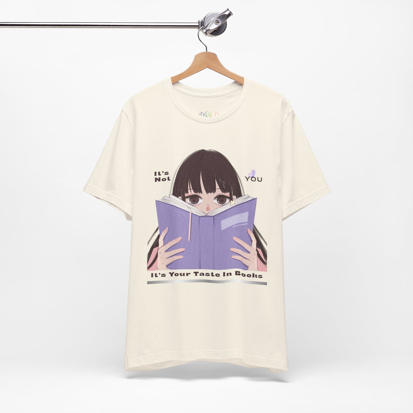 Beige t-shirt with graphic design of a girl peeking over the top of a book and text 'It's Not You. It's Your Taste In Books.'
