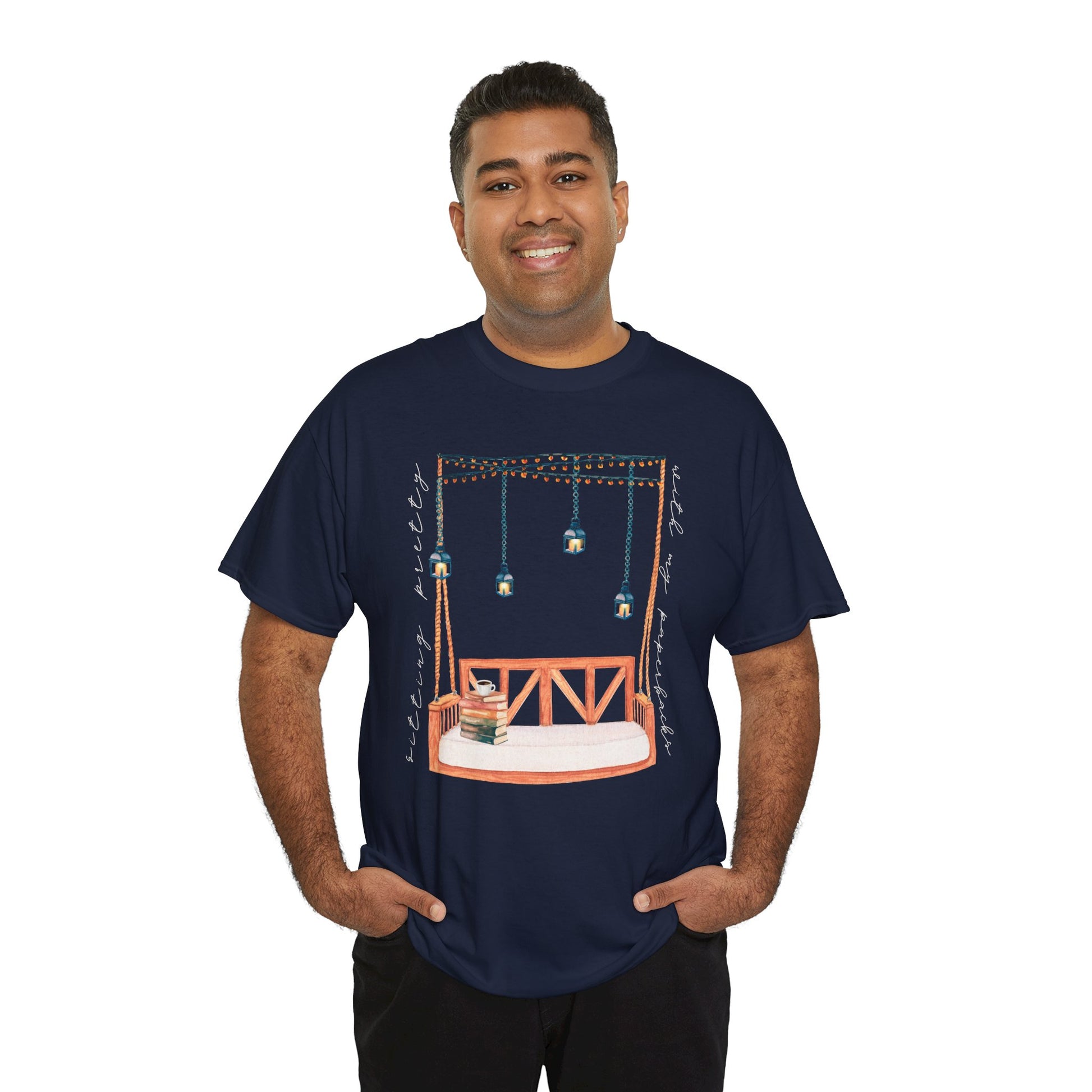 Man wearing a navy blue t-shirt with a porch swing, string lights, hot beverage and a stack of books, text says 'Sitting Pretty With My Paperbacks'