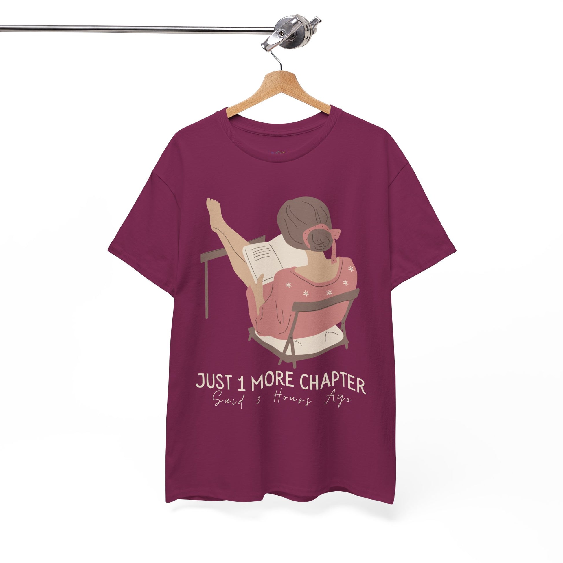 Berry t-shirt with a graphic of a person reading a book with her feet propped up and text 'Just 1 More Chapter, Read's Hours Ago' 