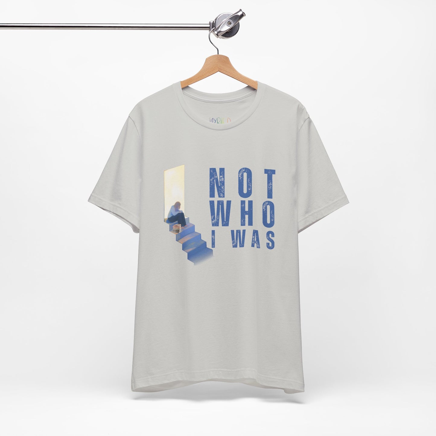 Light gray t-shirt with person sitting at the top of the stairs, lit from behind and text 'Not Who I Was'