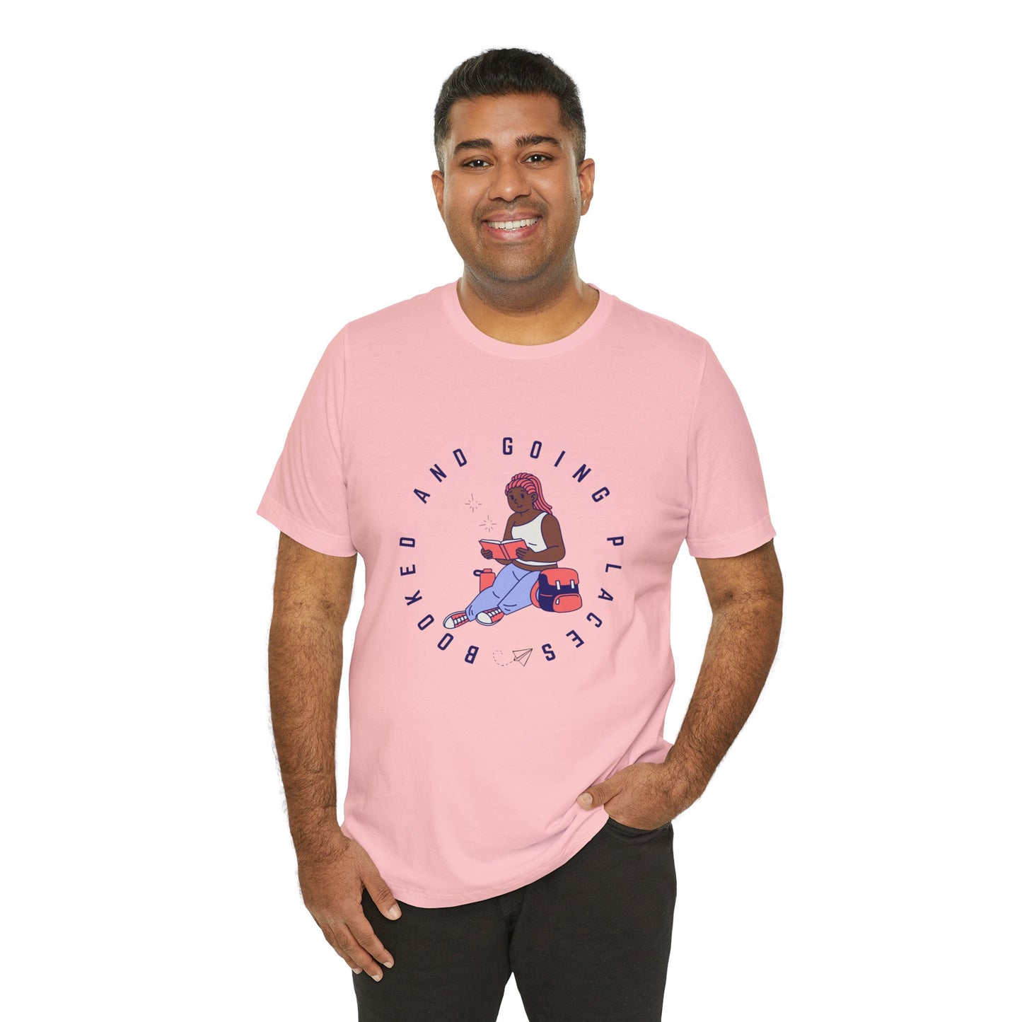 Man wearing a pink t-shirt with graphic design of a school girl sitting with a book and text 'Booked And Going Places'