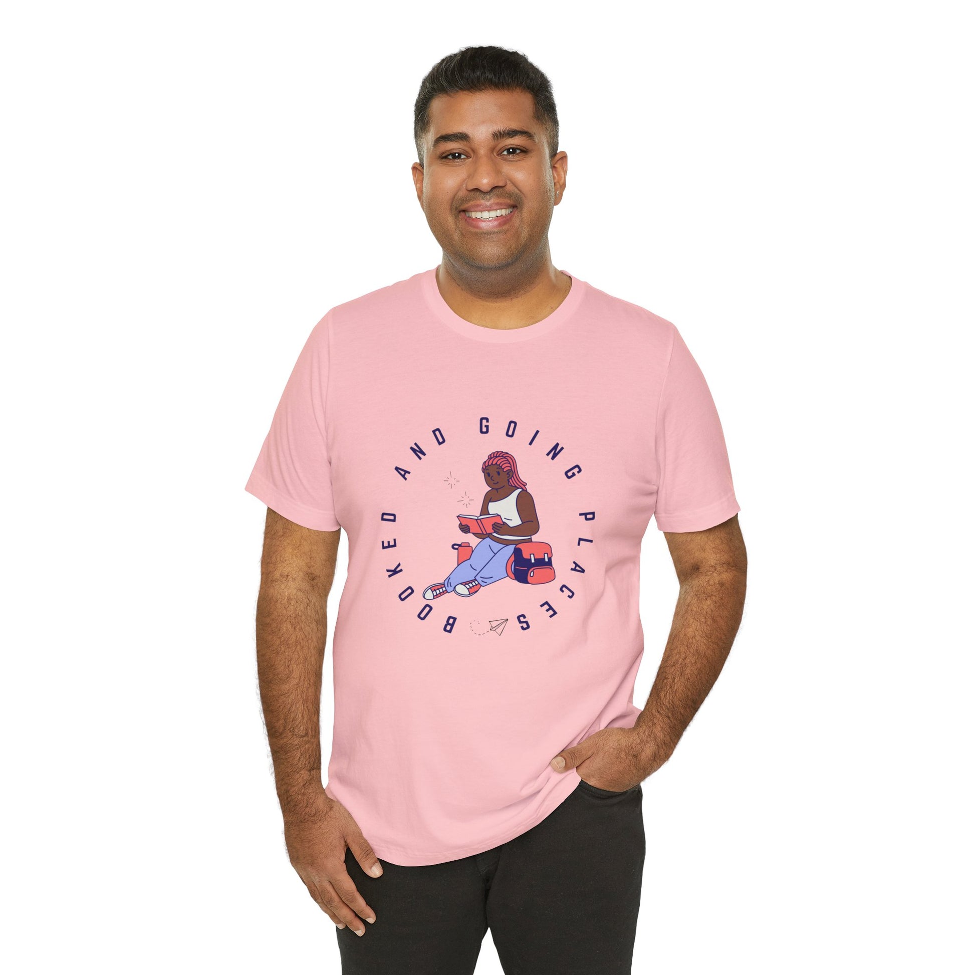 Man wearing a pink t-shirt with graphic design of a school girl sitting with a book and text 'Booked And Going Places'