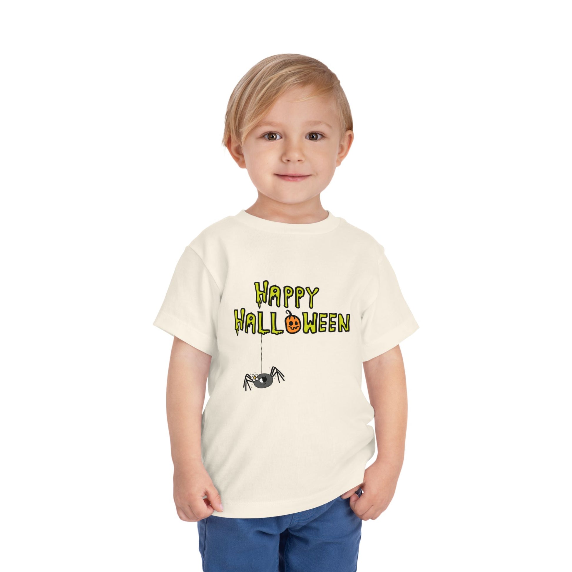 Toddler wearing a beige t-shirt with creepy type text 'Happy Halloween' and a dangling spider 