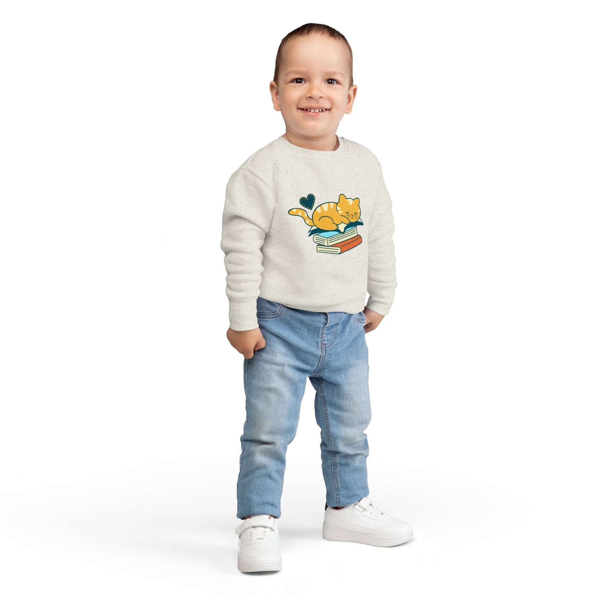 Boy wearing a beige toddler sweatshirt with a cat and snoozing on a stack of books