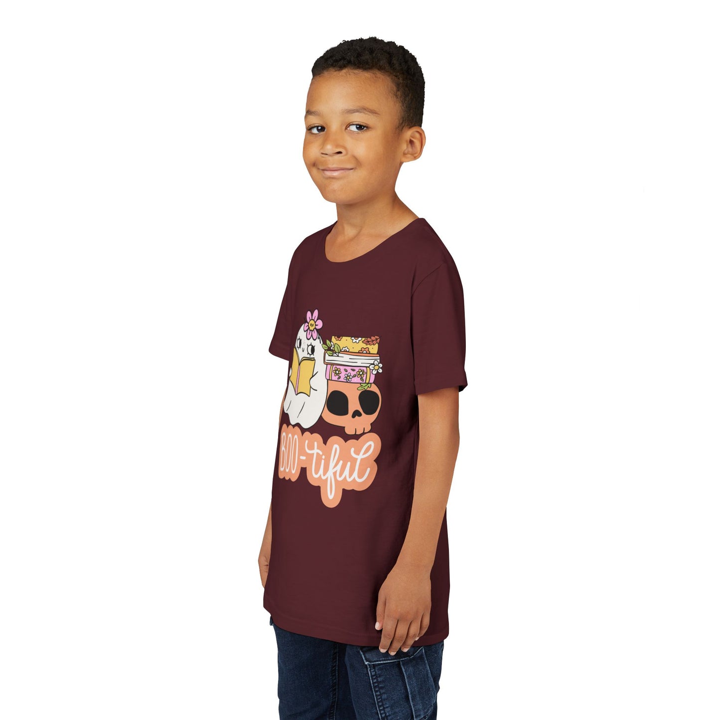 Boy wearing a maroon t-shirt with cartoon ghost leaning on a skull and stack of books while reading and text 'BOO-tiful'