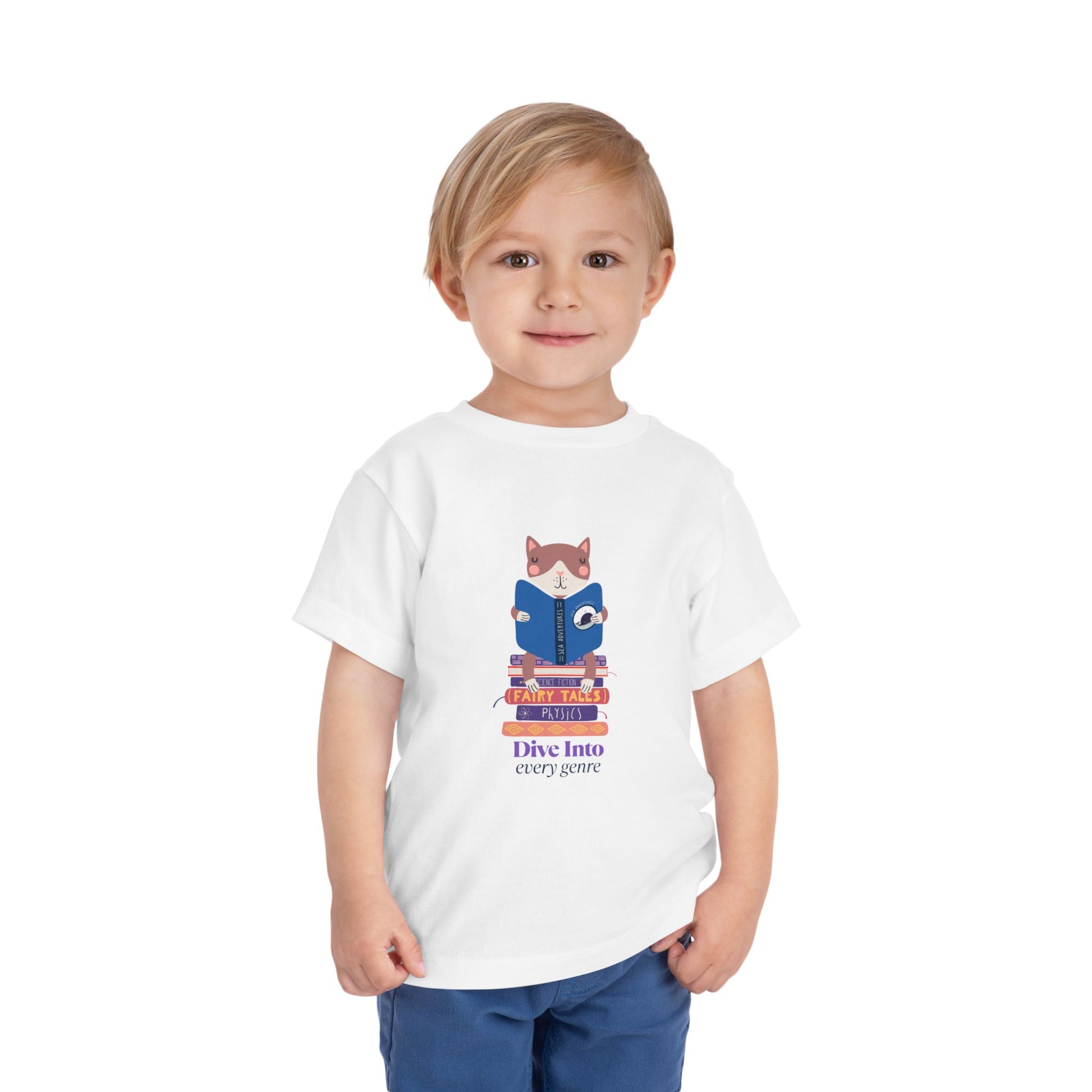 Child wearing a white toddler t-shirt with a cat reading a book while sitting on a stack of books and text 'Dive Into Every Genre'