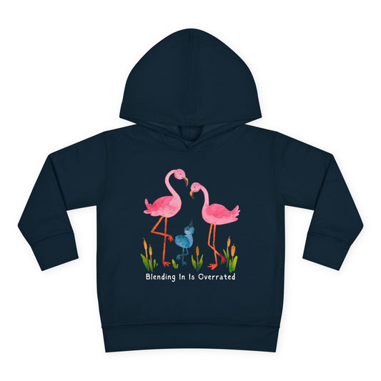 Two pink flamingos standing beside a bright blue bird, with the words “Blending In Is Overrated” above — printed on a toddler hoodie.