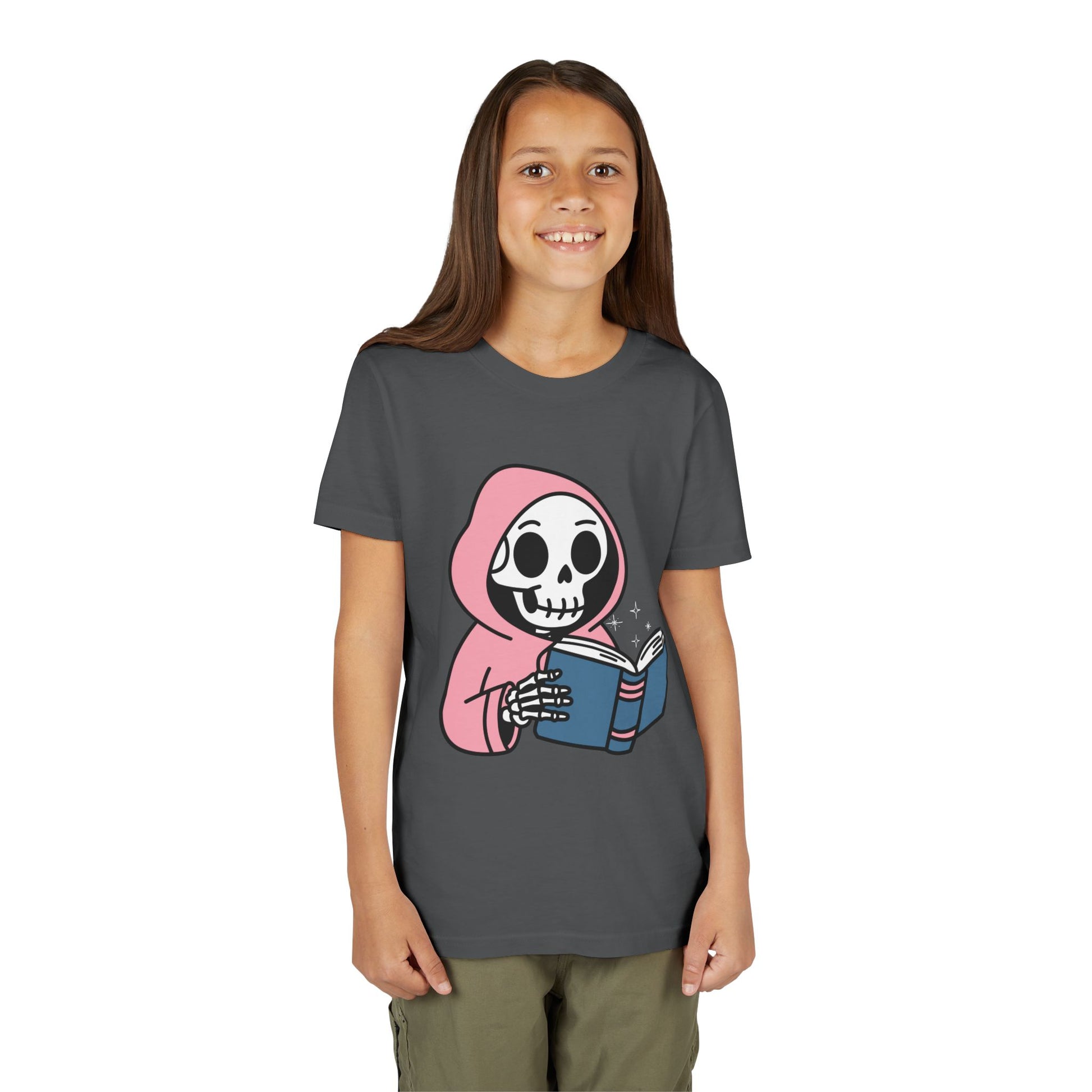 Girl wearing a gray t-shirt with a cartoon skeleton wearing a pink hoodie and reading a book