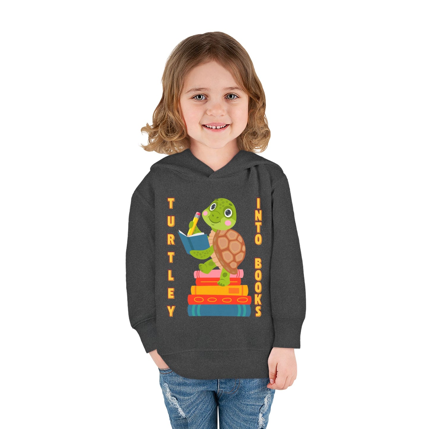 Girl wearing a dark gray toddler hoodie with a turtle graphic, notebook, stack of books and text 'Turtley Into Books'