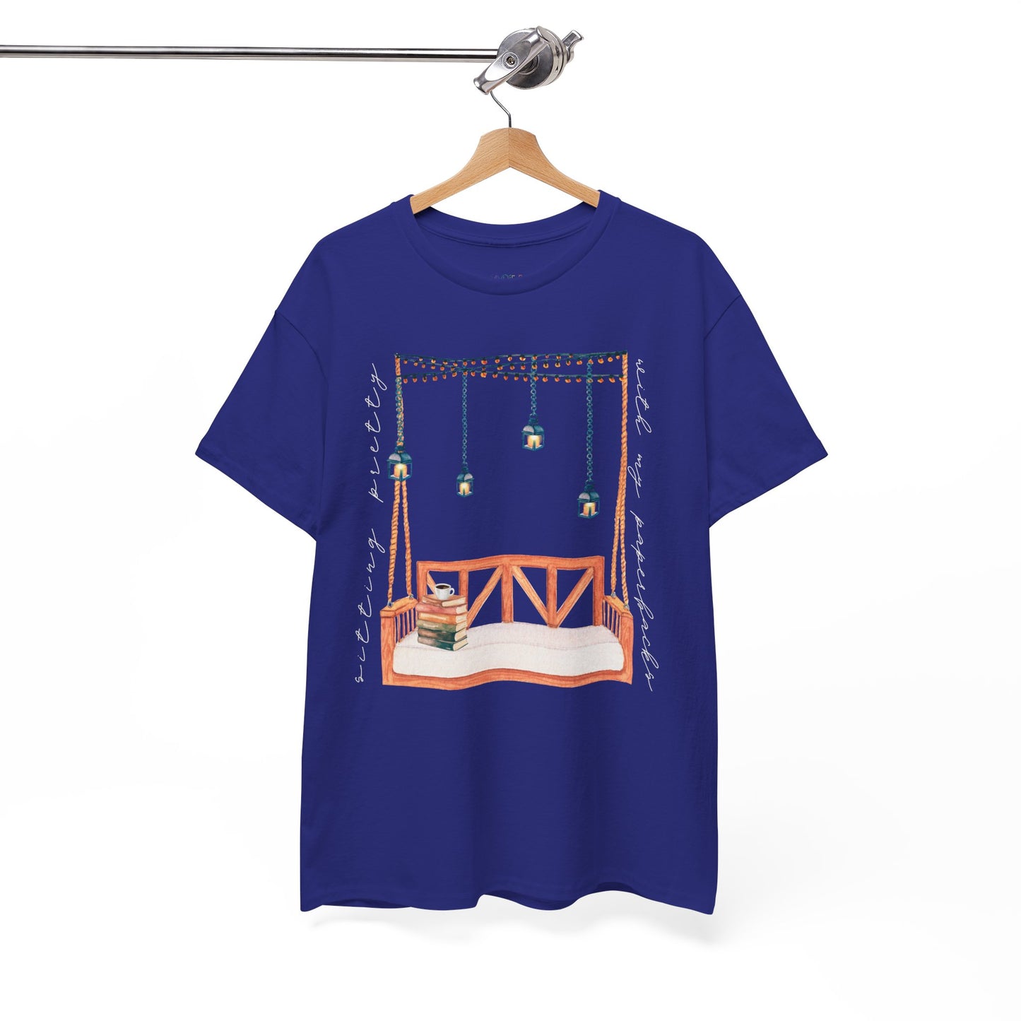 Blue t-shirt with a porch swing, string lights, hot beverage and a stack of books, text says 'Sitting Pretty With My Paperbacks'