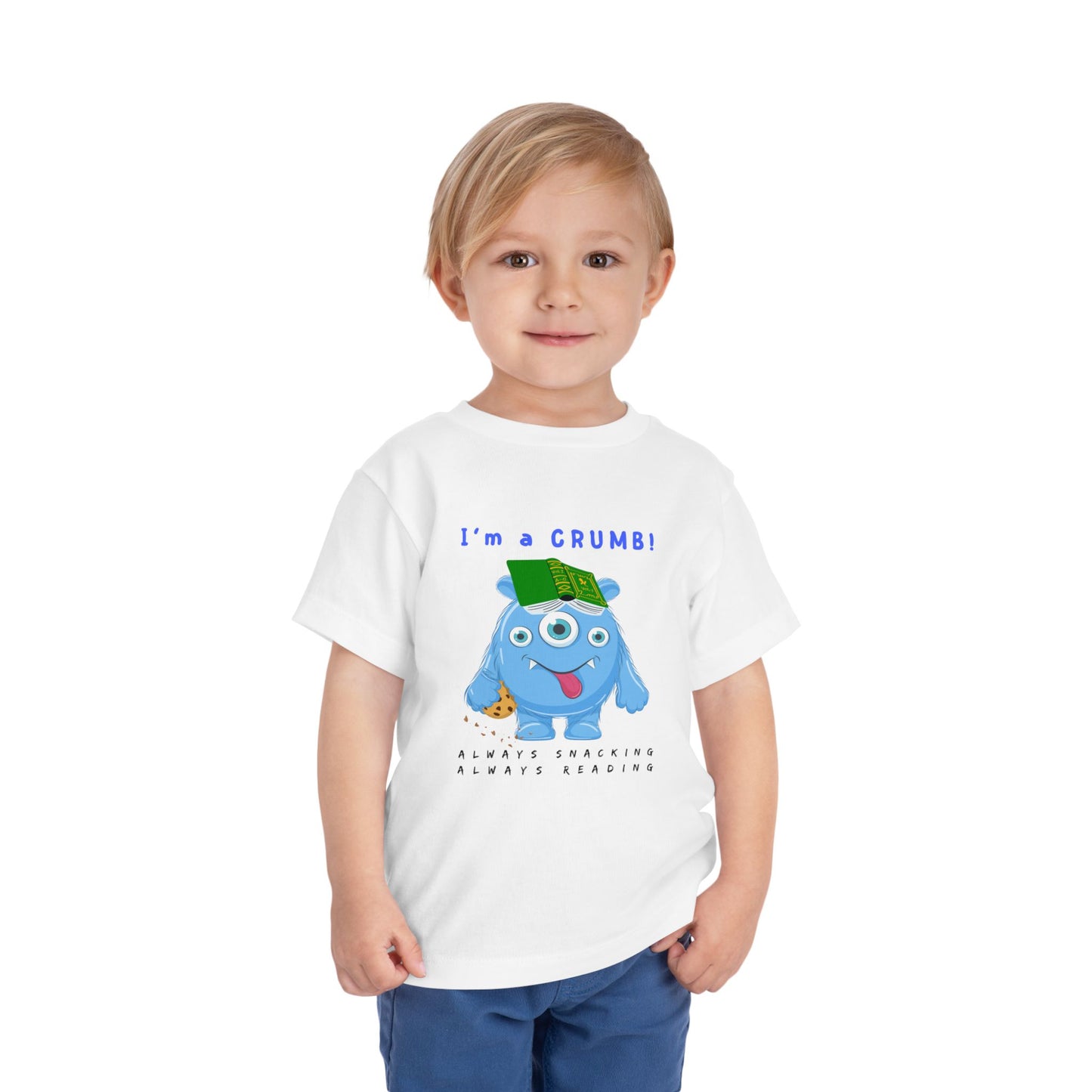 Child wearing a white toddler personality t-shirt with a blue cartoon monster eating a cookie and wearing a book on it's head, proudly proclaiming 'I'm A Crumb!' Sub-text 'Always Snacking, Always Reading' on a white background