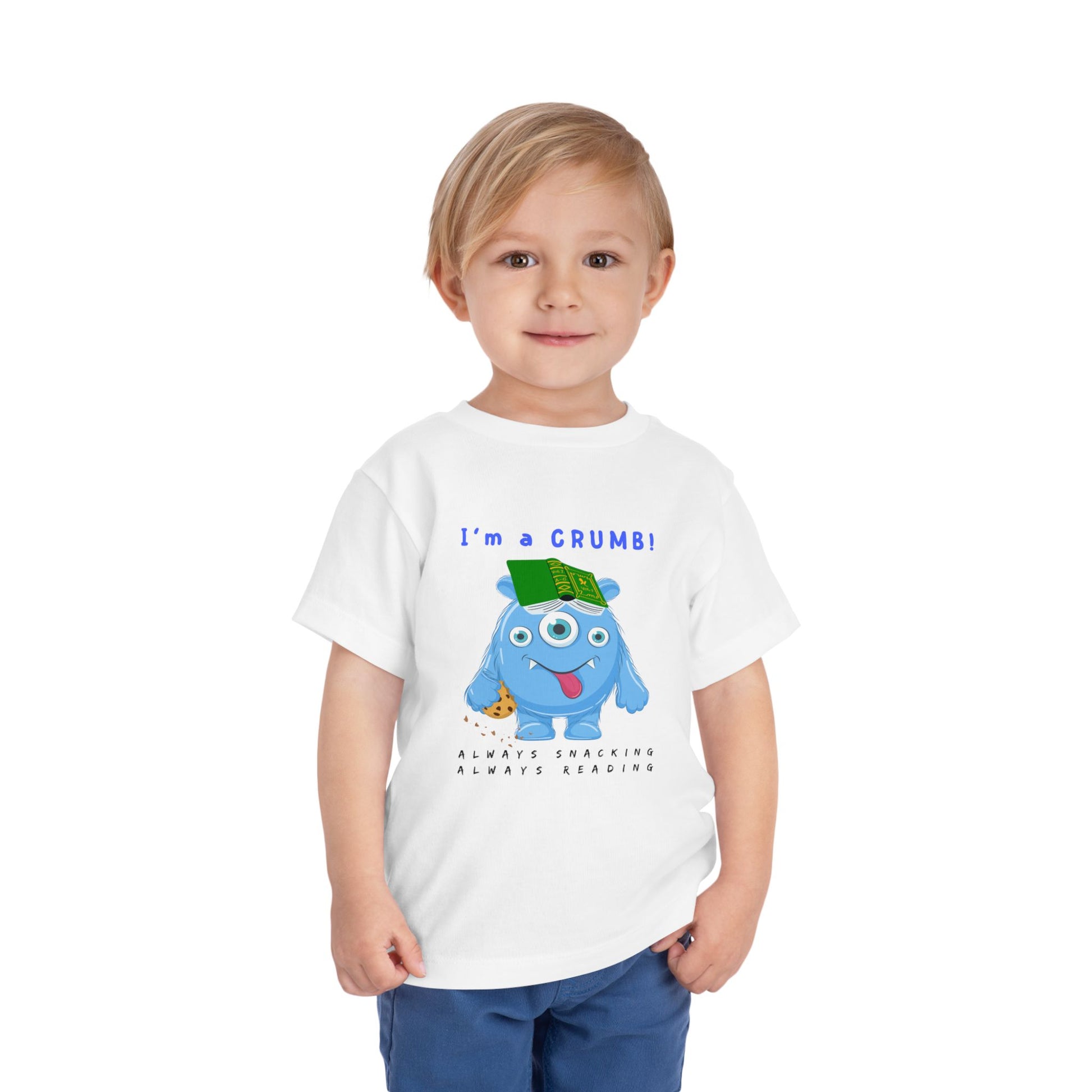 Child wearing a white toddler personality t-shirt with a blue cartoon monster eating a cookie and wearing a book on it's head, proudly proclaiming 'I'm A Crumb!' Sub-text 'Always Snacking, Always Reading' on a white background