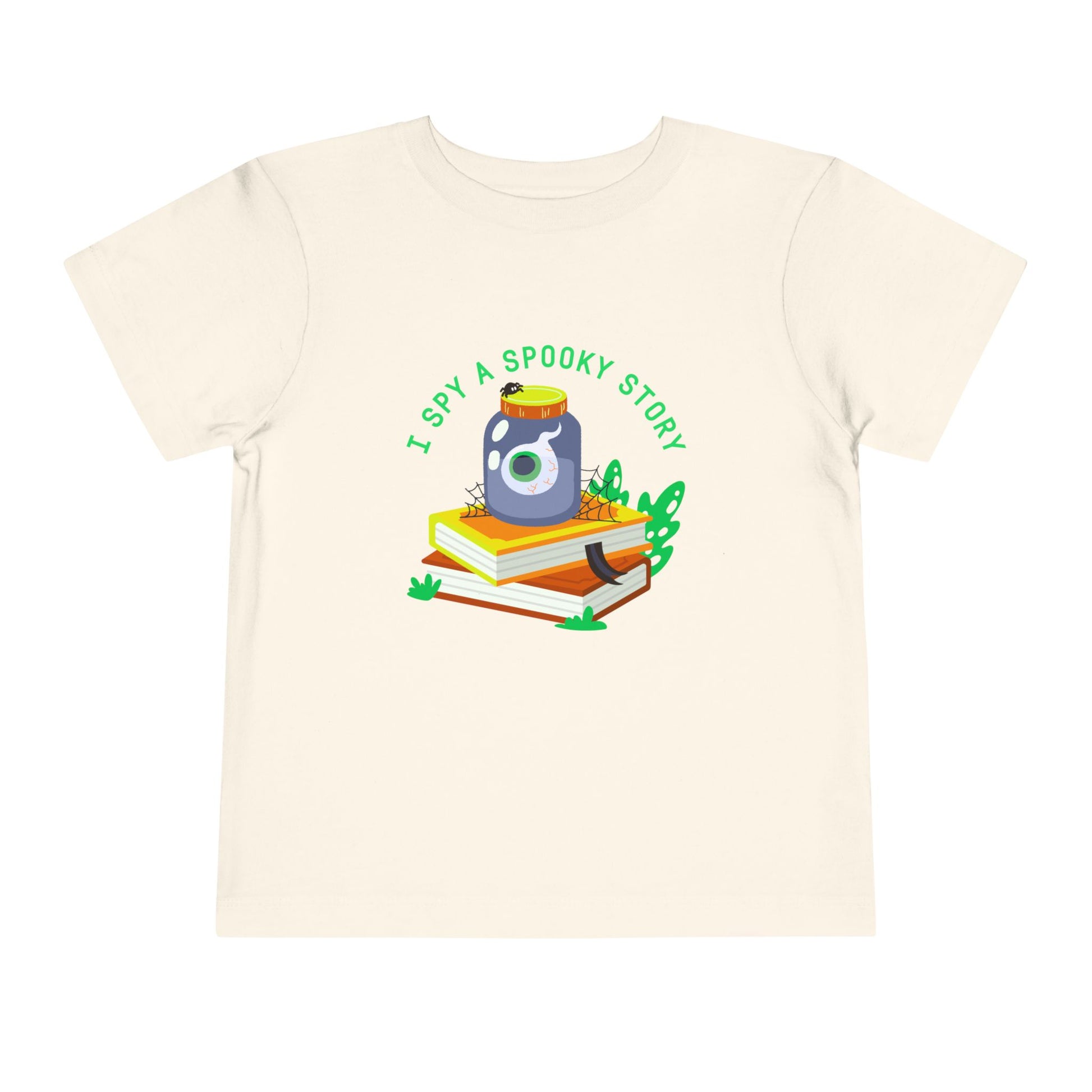 Beige toddler t-shirt with an eyeball in a yar on top of books and text 'I spy a spooky story' on a white background