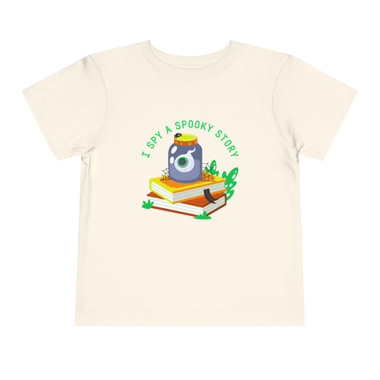 Beige toddler t-shirt with an eyeball in a yar on top of books and text 'I spy a spooky story' on a white background