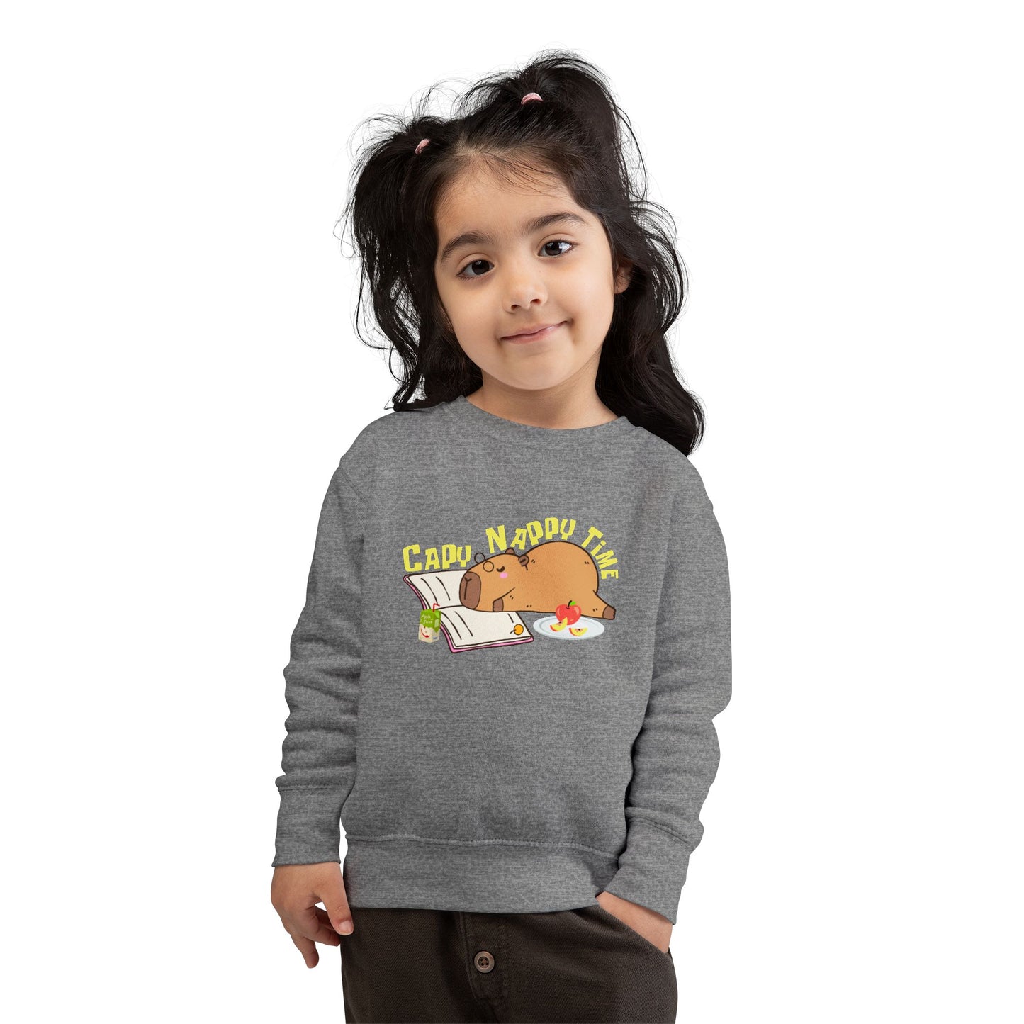Girl wearing a gray toddler sweatshirt with a napping capybara, snacks, an open book and text 'Capo Nappy Time'