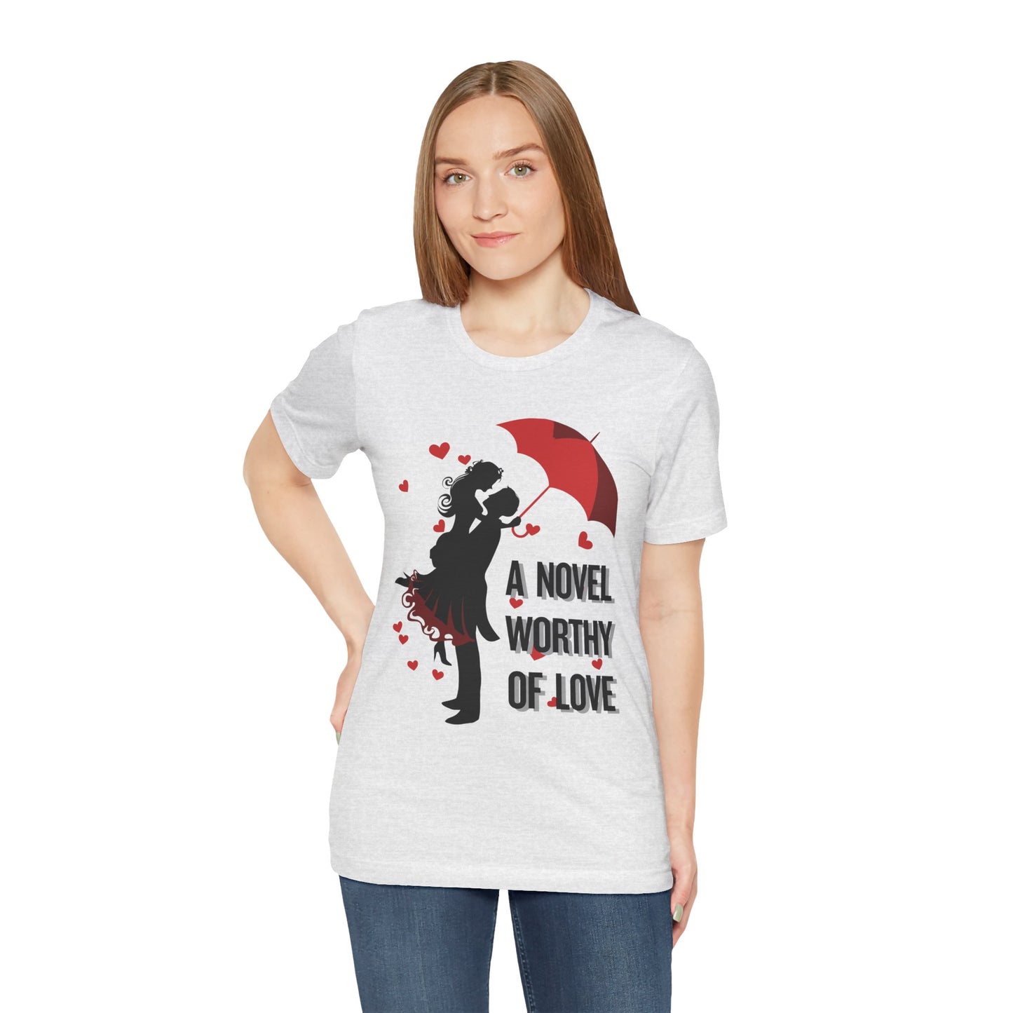 A woman wearing an ash t-shirt with a black graphic design of a man holding a woman under a red umbrella, sprinkled with hearts and text 'A Novel Worthy of Love' 