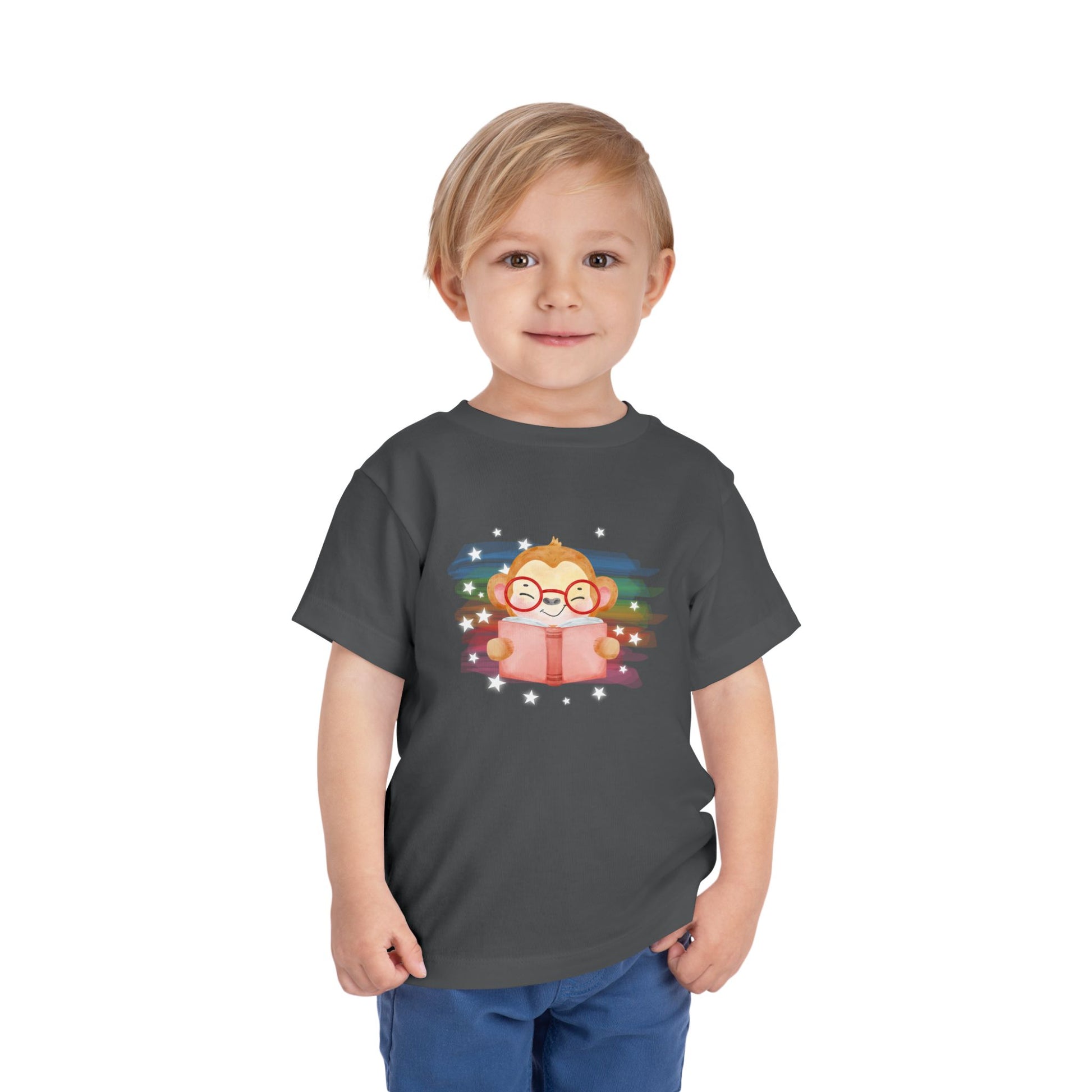 Toddler wearing a t-shirt with a cartoon monkey reading a book, lit up by rainbow watercolor rainbow and stars