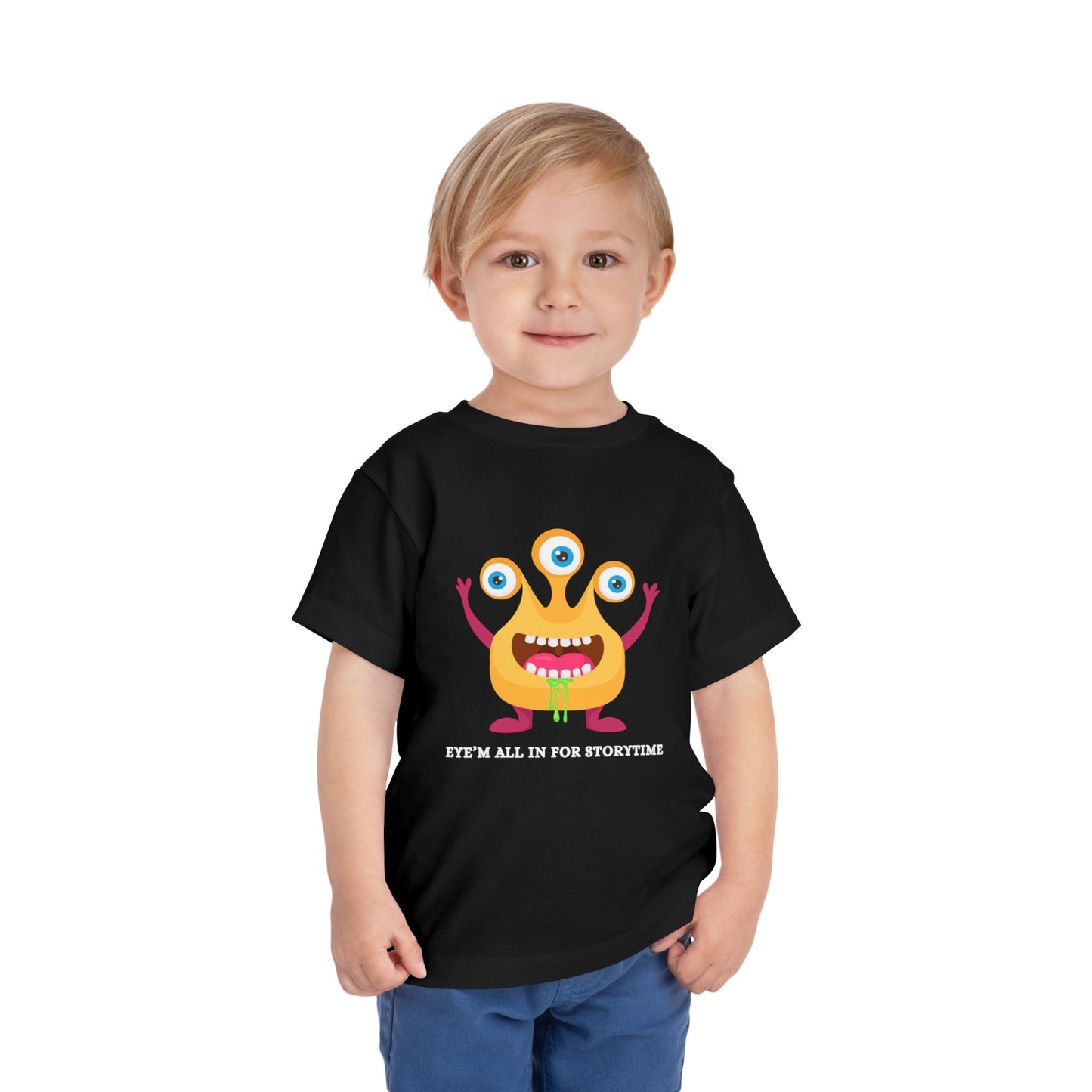 Child wearing a black toddler t-shirt with a drooling, three-eyed monster graphic and text 'Eye'm all in for storytime' on a white background