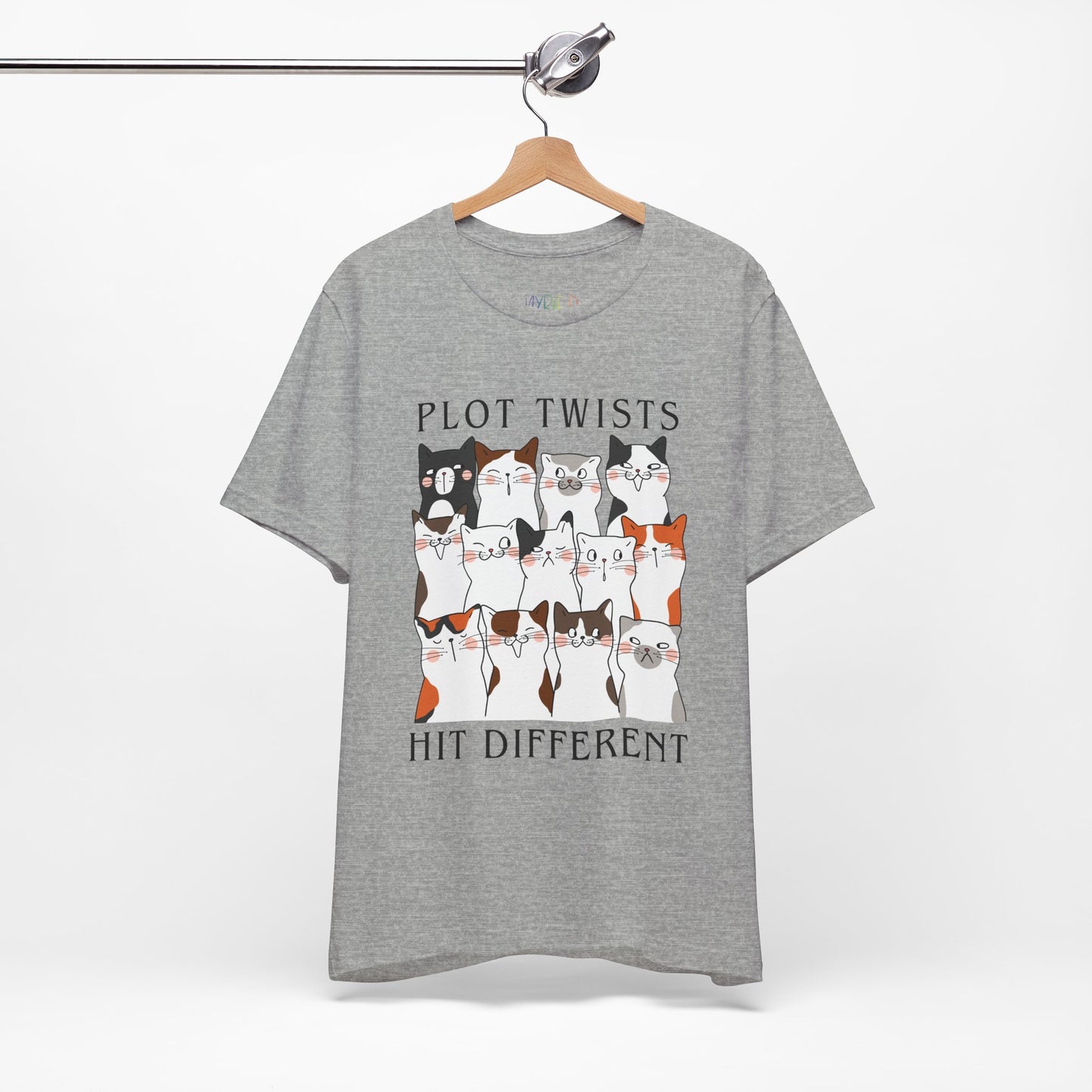 Gray t-shirt with rows of cats making different faces and text 'Plot Twists Hit Different' 