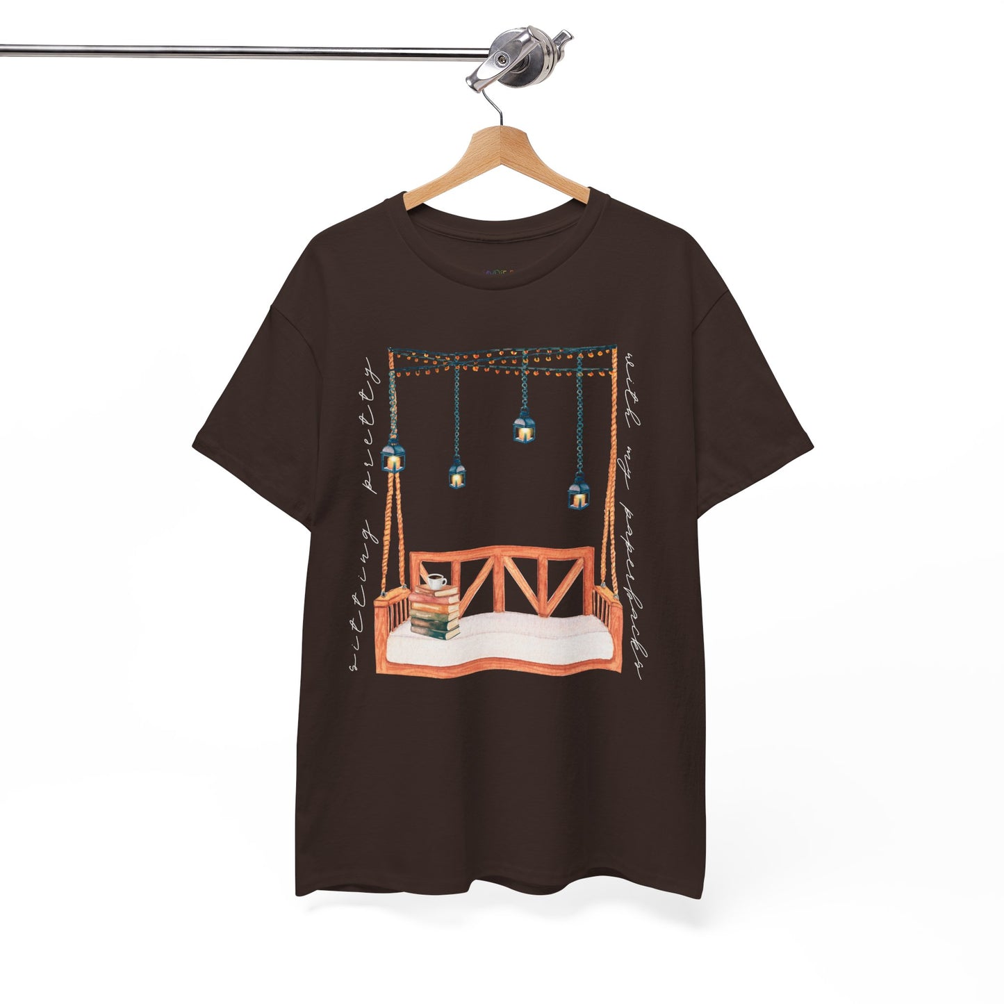Brown t-shirt with a porch swing, string lights, hot beverage and a stack of books, text says 'Sitting Pretty With My Paperbacks'