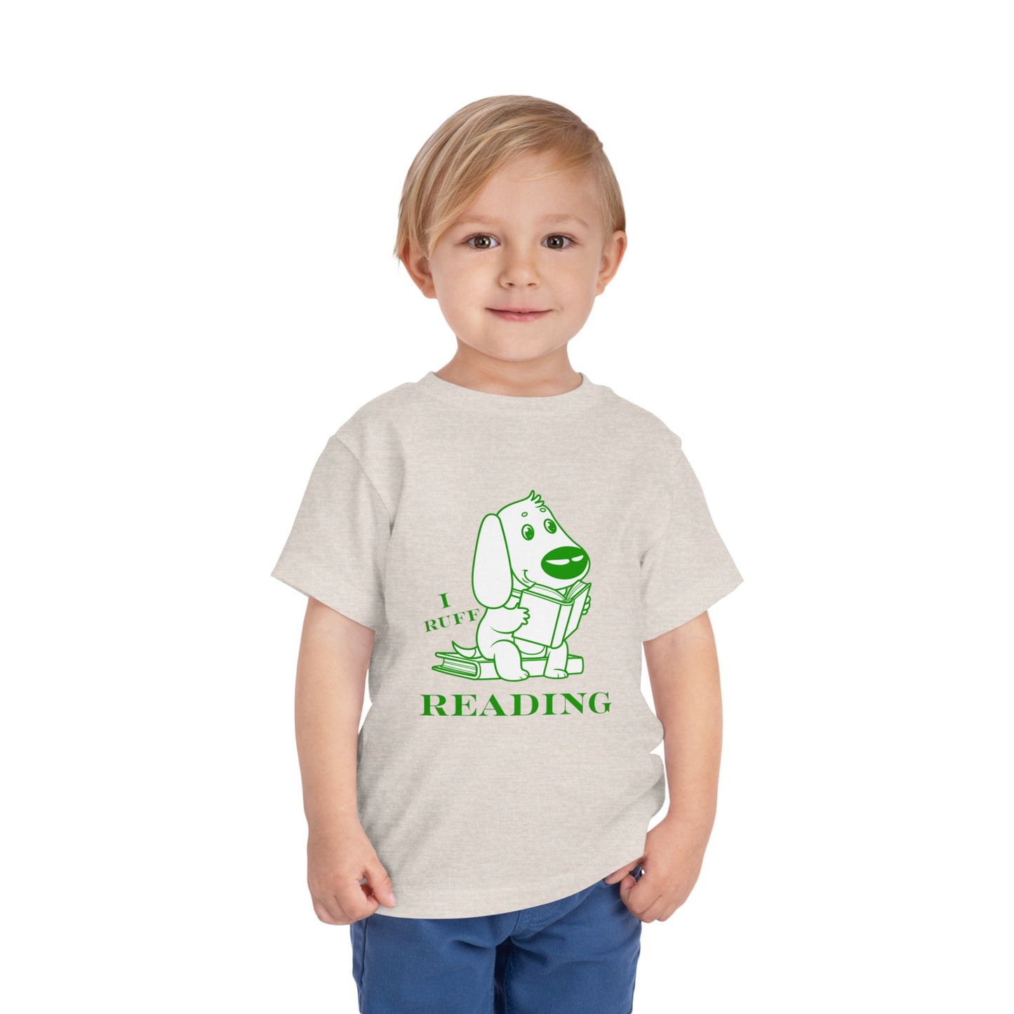 Child wearing a beige toddler t-shirt with green and white graphic of a dog reading a book and text 'I RUFF READING'
