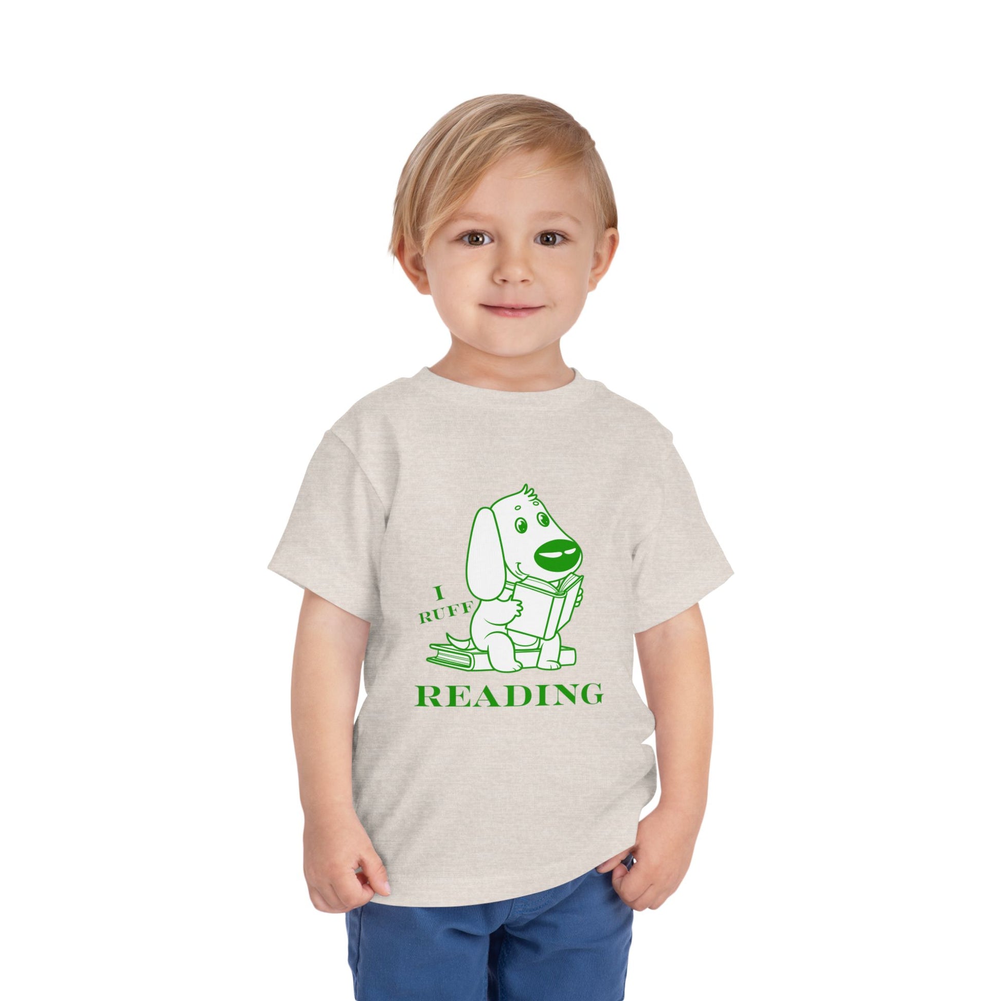 Child wearing a beige toddler t-shirt with green and white graphic of a dog reading a book and text 'I RUFF READING'
