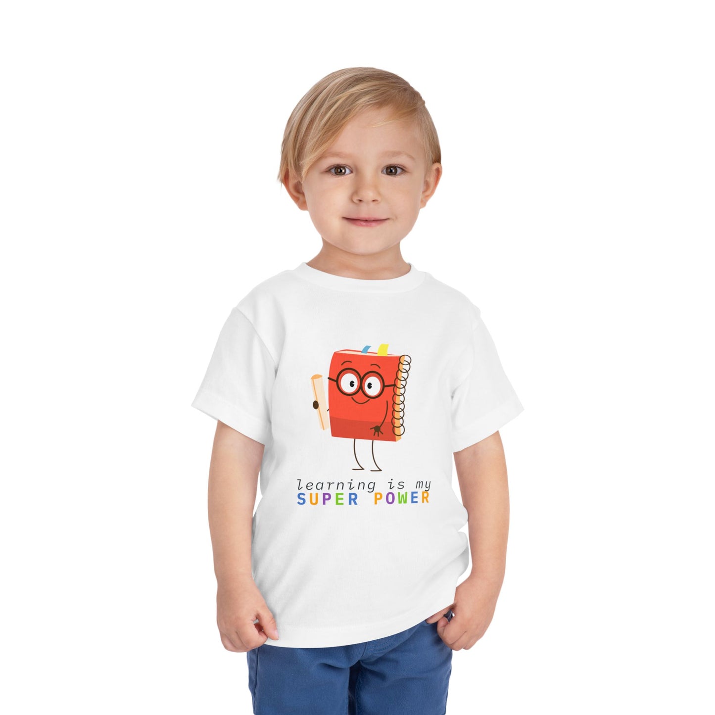 Child wearing a white toddler t-shirt with a cartoon book character and colorful 'learning is my super power' text 
