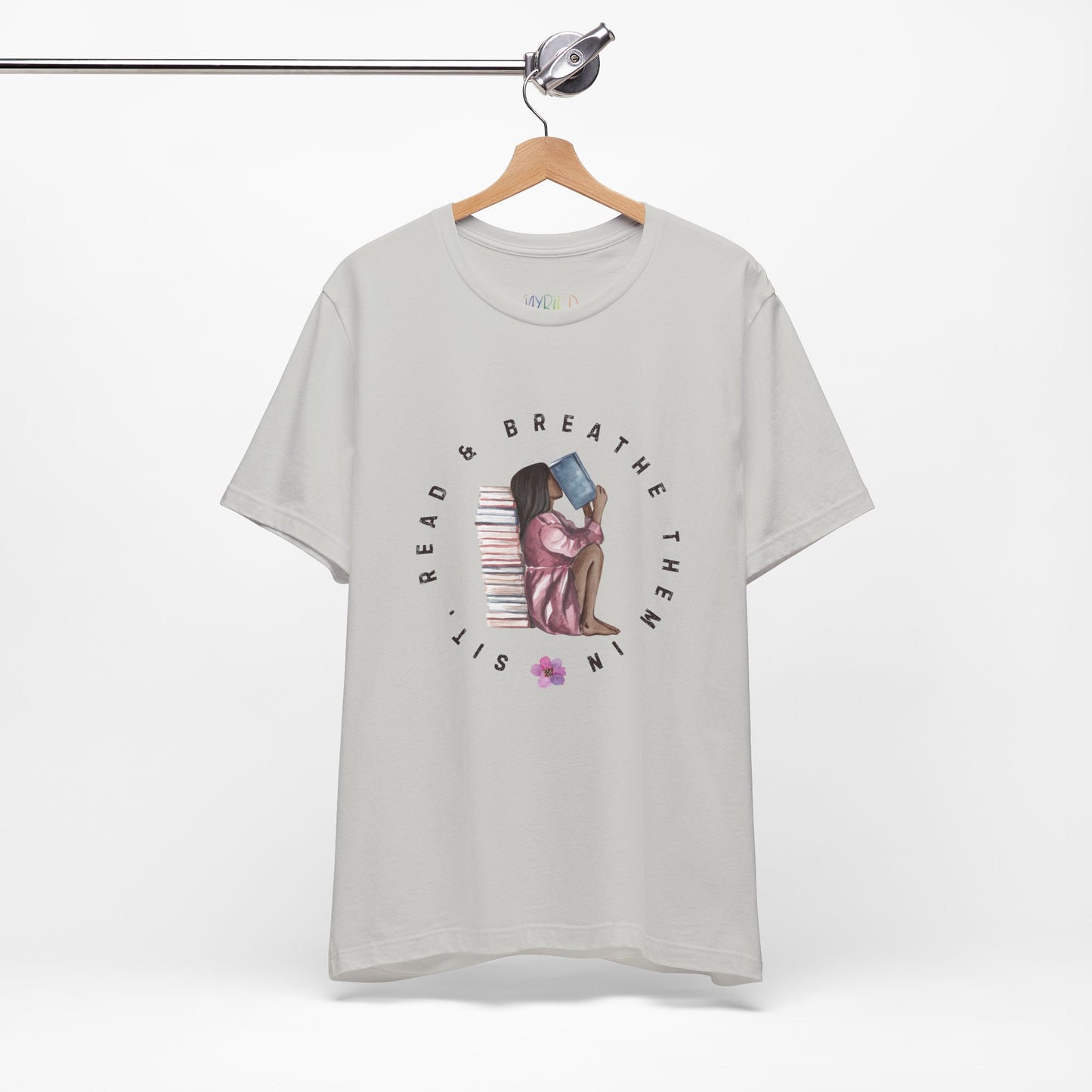 light gray t-shirt with graphic design of a girl sitting on the ground against a stack of books, inhaling the book she's reading and text 'Sit, Read & Breathe Them In'
