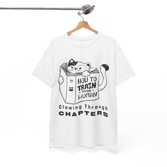 White t-shirt with black graphic design of a cat reading a 'How To Train Your Human' book and text 'Clawing Through Chapters'