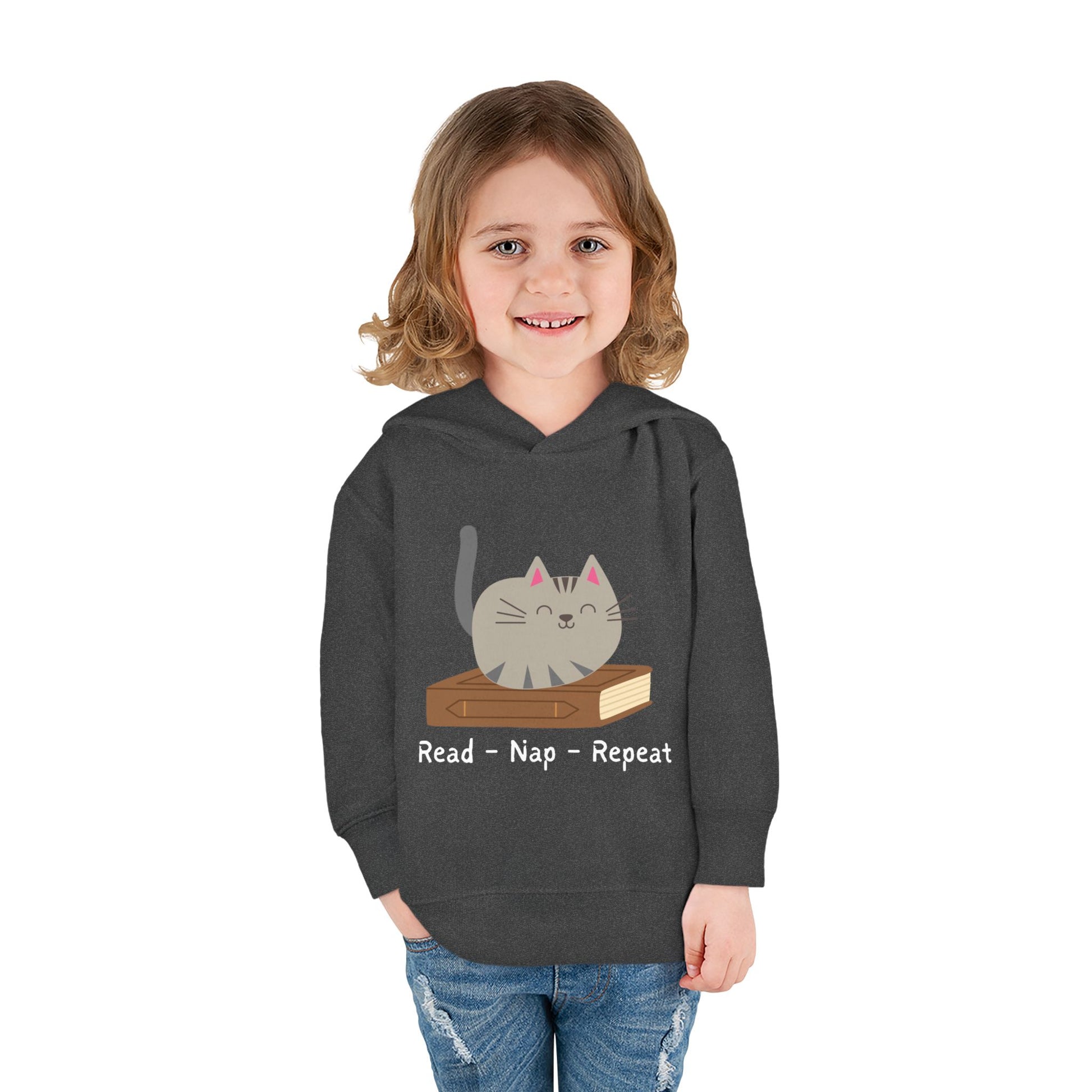 Girl wearing a dark gray toddler hoodie featuring a gray cat laying on a book and text 'Read - Nap - Repeat' on a white background