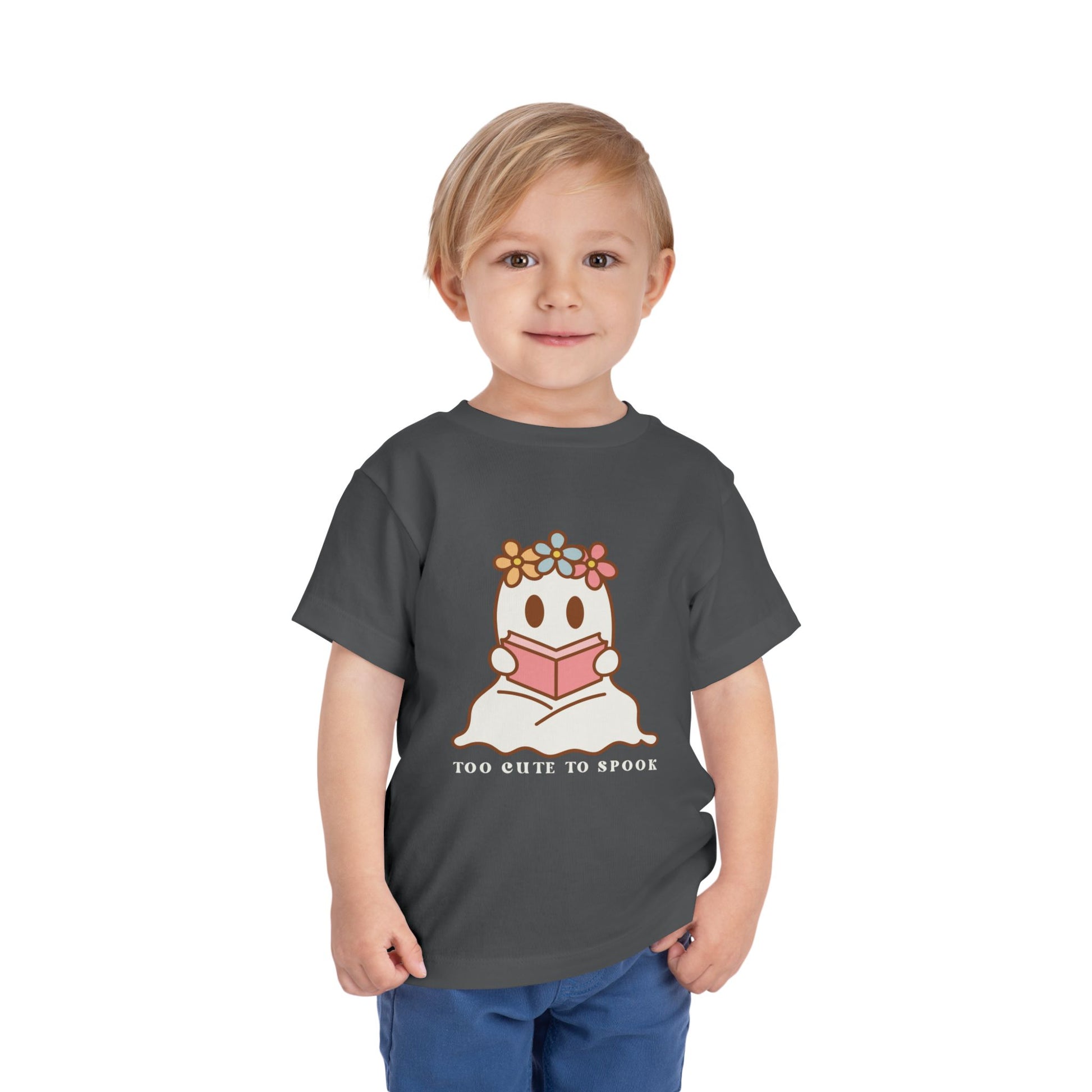 Child wearing a gray toddler t-shirt with a ghost reading a book and 'Too Cute to Spook' text on a white background