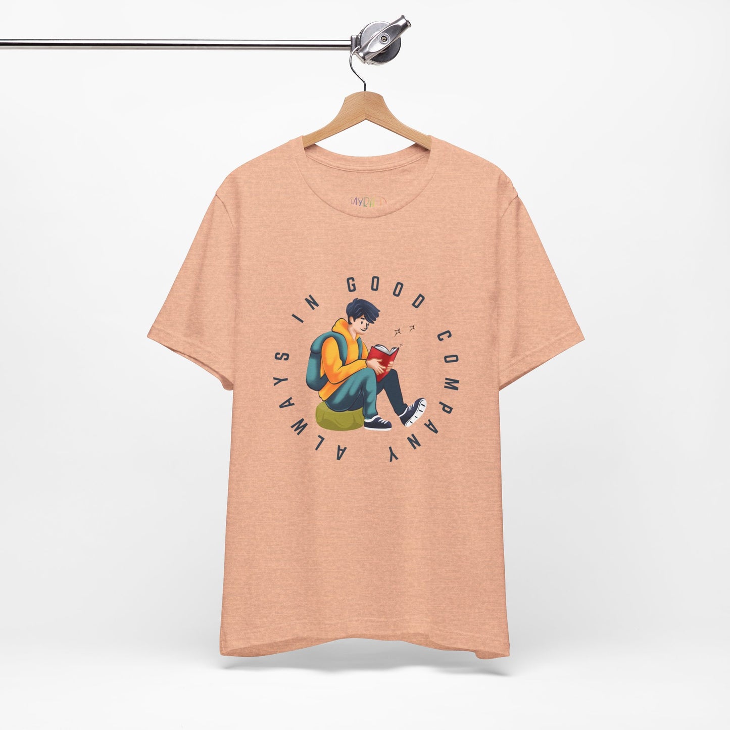 Peach t-shirt with a graphic design of a person reading a book, sitting on a green bag, with text 'Always In Good Company' 