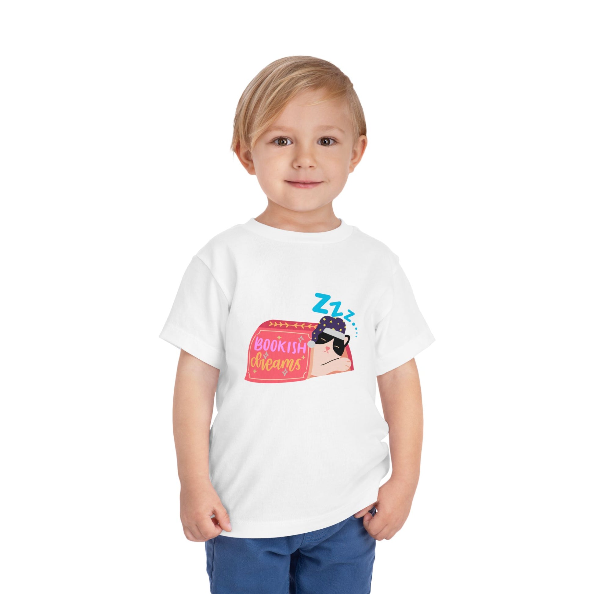 Child wearing a white toddler t-shirt with a snoozing cat in a night cap, under a book and text 'Bookish Dreams' 