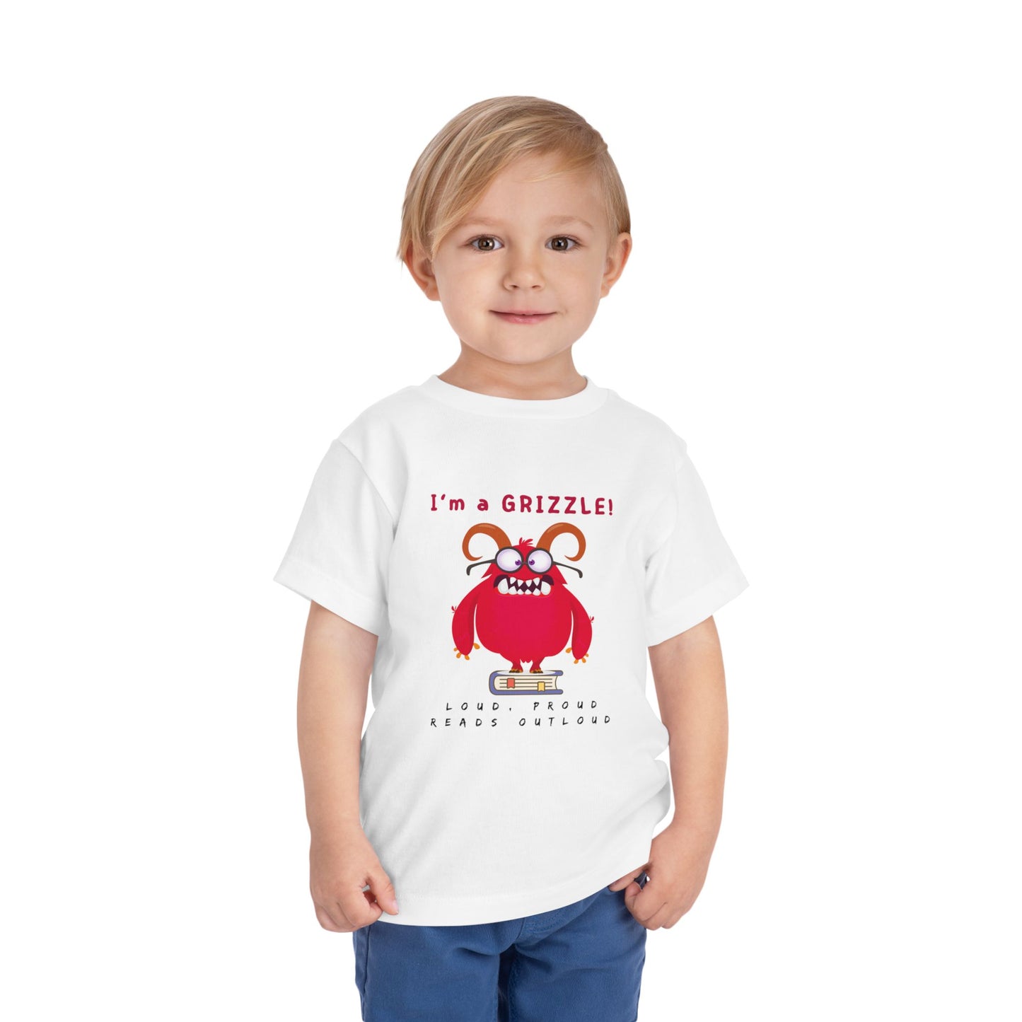 Child wearing a white toddler personality t-shirt with a red monster graphic standing on a book proudly proclaiming 'I'm a GRIZZLE!' Sub-text 'Loud, Proud, Reads Aloud.'