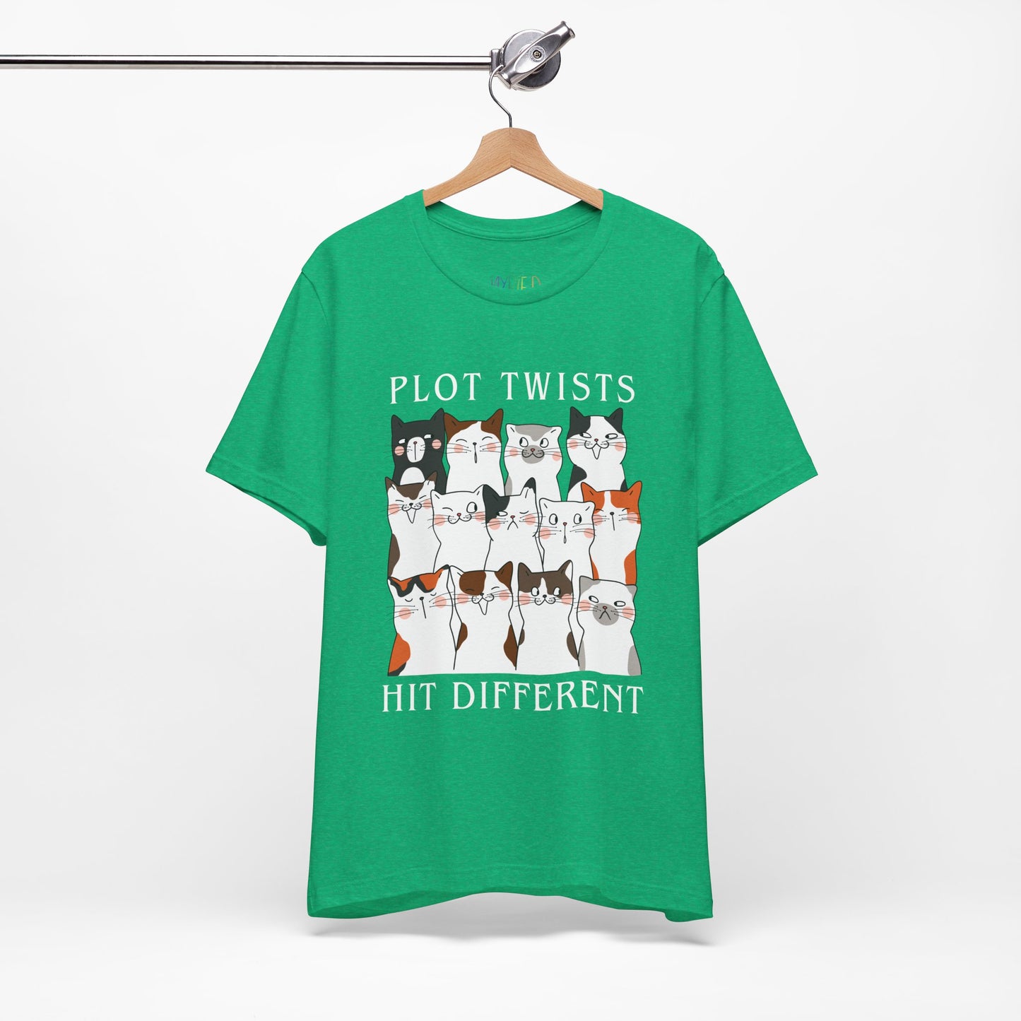 Green t-shirt with rows of cats making different faces and text 'Plot Twists Hit Different' 