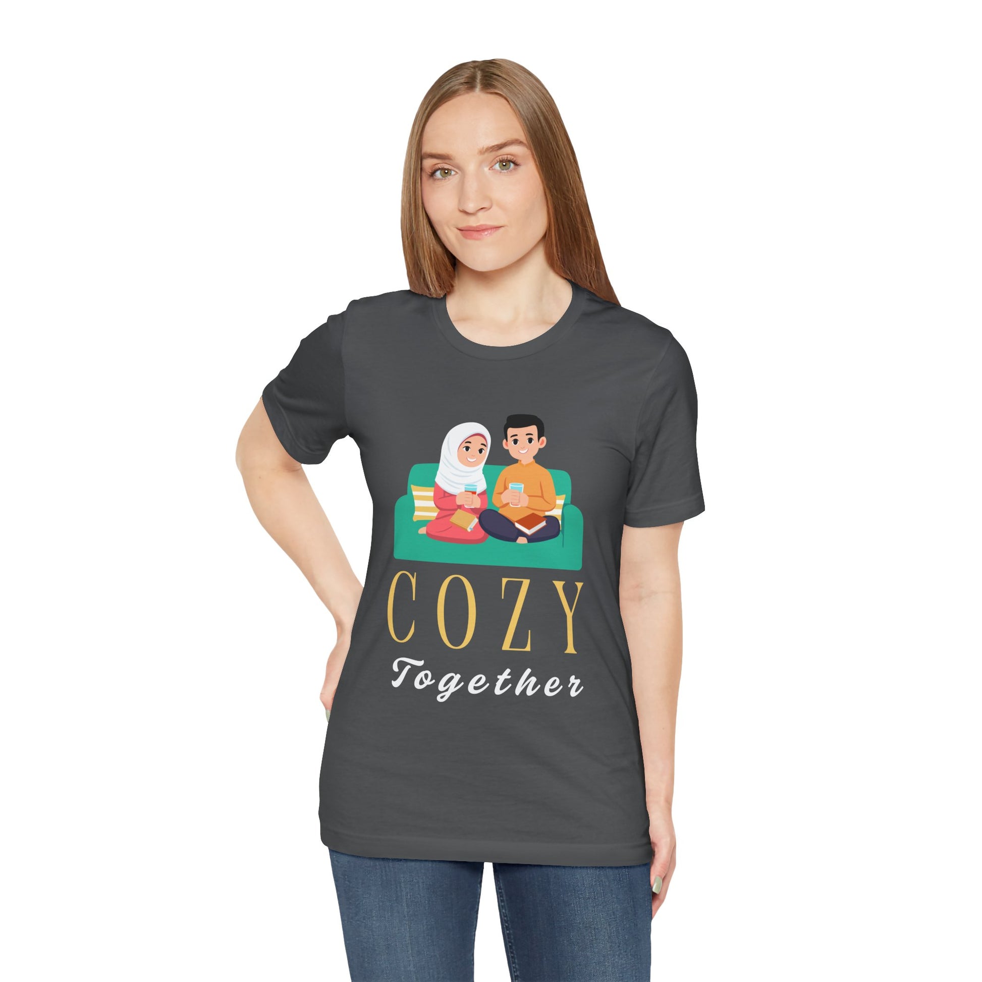 Woman wearing a gray t-shirt with a graphic of two people on a couch, with books and drinks, the text 'Cozy Together' sits beneath in large letters